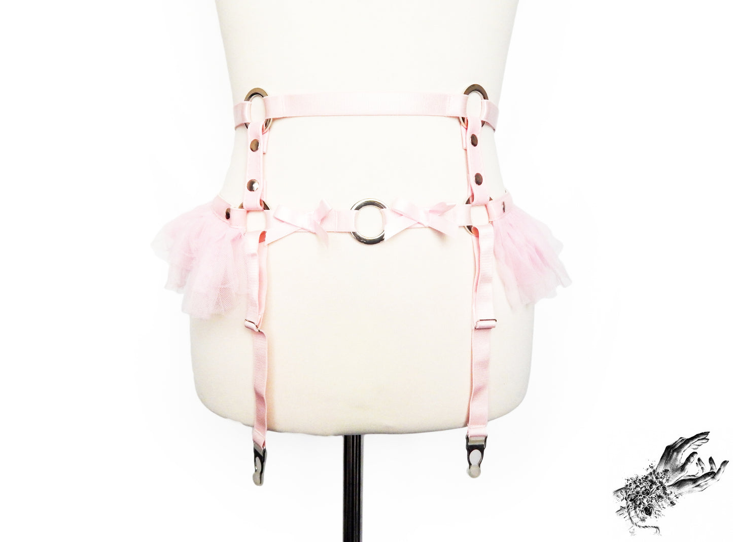 Pink vegan leather garter belt featuring silver O ring hardware, pink ruffled tulle and bow appliques, displayed on a mannequin against a white background.