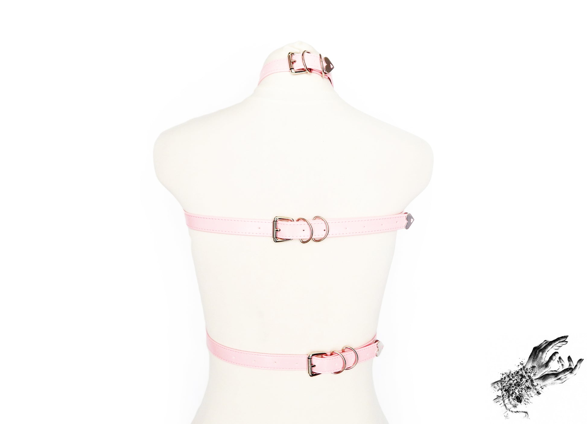 Rear view of a pink vegan leather top harness featuring silver O ring hardware and adjustable neck, chest and waist straps, displayed on a mannequin against a white background.