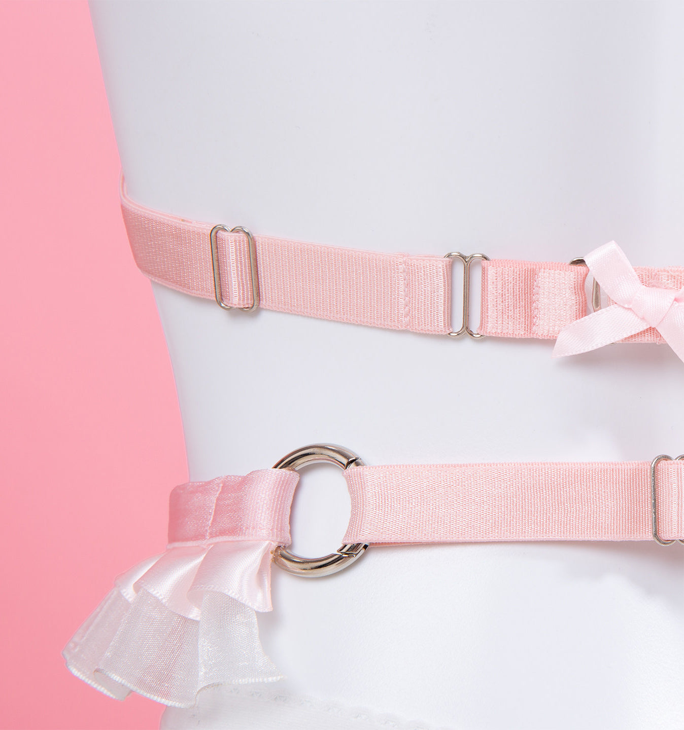 Pink satin elastic waist and hip straps with silver metal hardware, displayed on a white mannequin torso against a pink and white background.