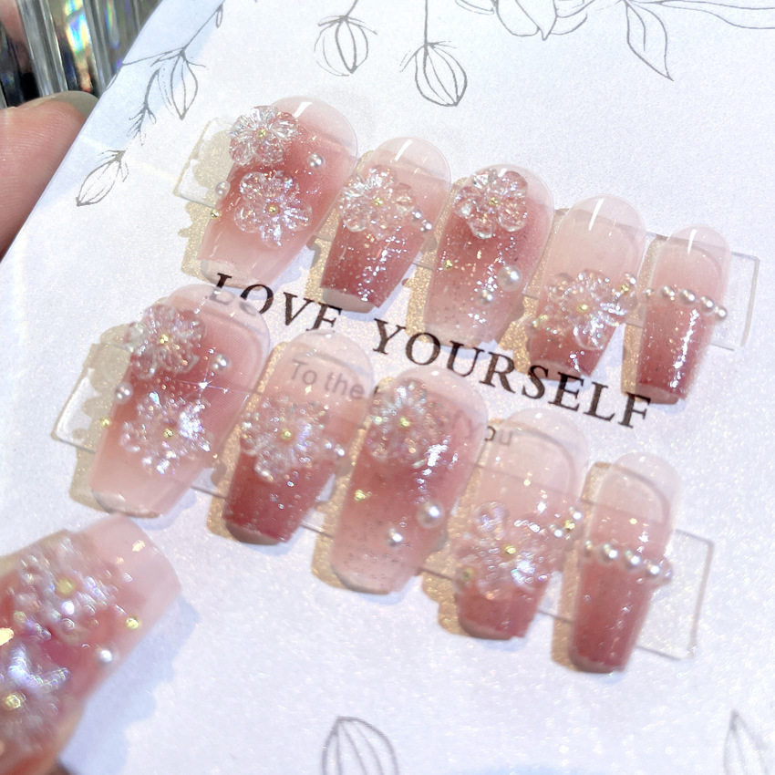 medium length ballerina tip nude and pink glitter false nails featuring 3D sculpted gel flowers and white pearl beads, displayed on a white floral backing card.