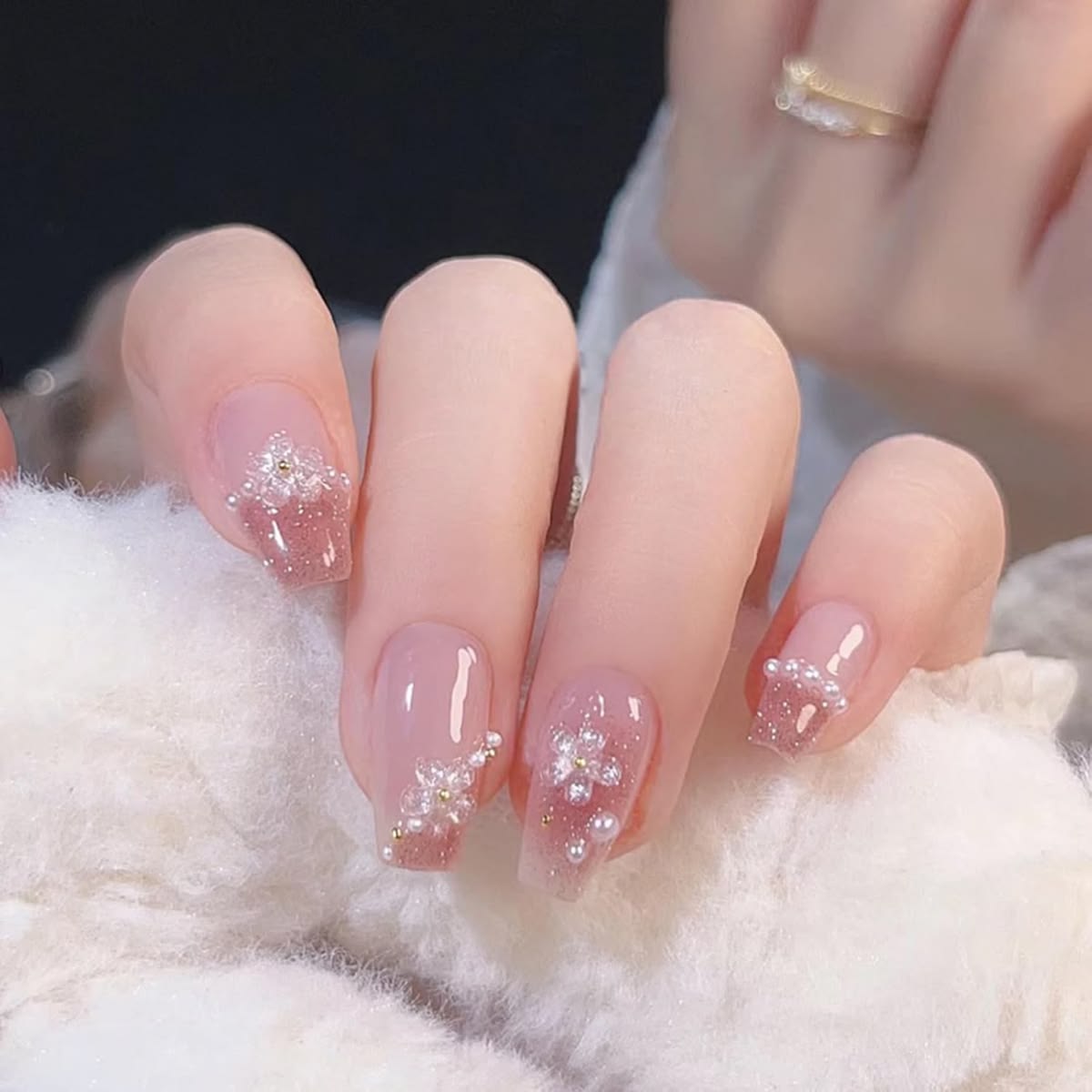 nude and pink glitter false nails featuring 3D sculpted gel flowers and white pearl beads, modelled on a hand wearing a white fur coat.