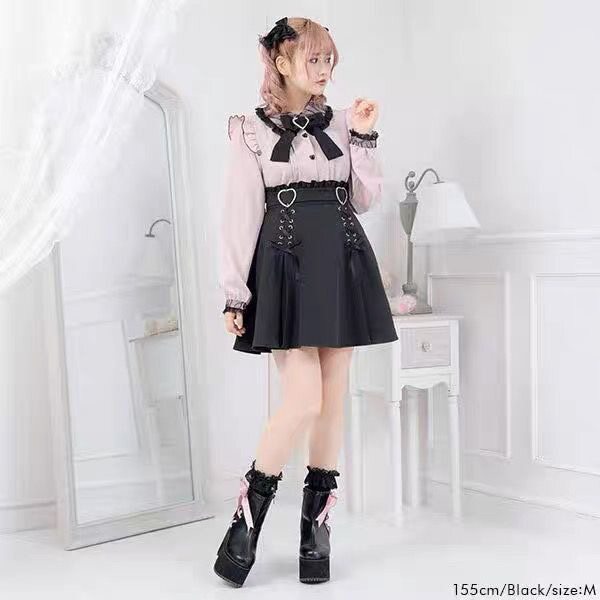 Modelled photo of a pink and black long sleeved blouse featuring a Peter Pan collar, ruffled shoulders, pintucks, heart shaped buttons and detachable bow brooch. Styled with a black ruffled skirt and boots for a Jirai Kei aesthetic.