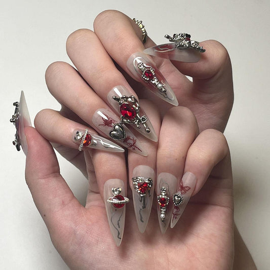 Long stiletto length false nails featuring white and red blended bases with silver swirls and flames, red butterflies, 3D silver and red crystal heart, butterfly and star charms, modelled on a pair of hands against a white background.