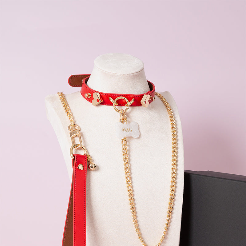 Red leather choker featuring gold tone hardware, custom engraved bone shaped pet tag, heavy duty chain leash and leather hand strap. Displayed on a white mannequin bust against a light pink background for a kawaii aesthetic.