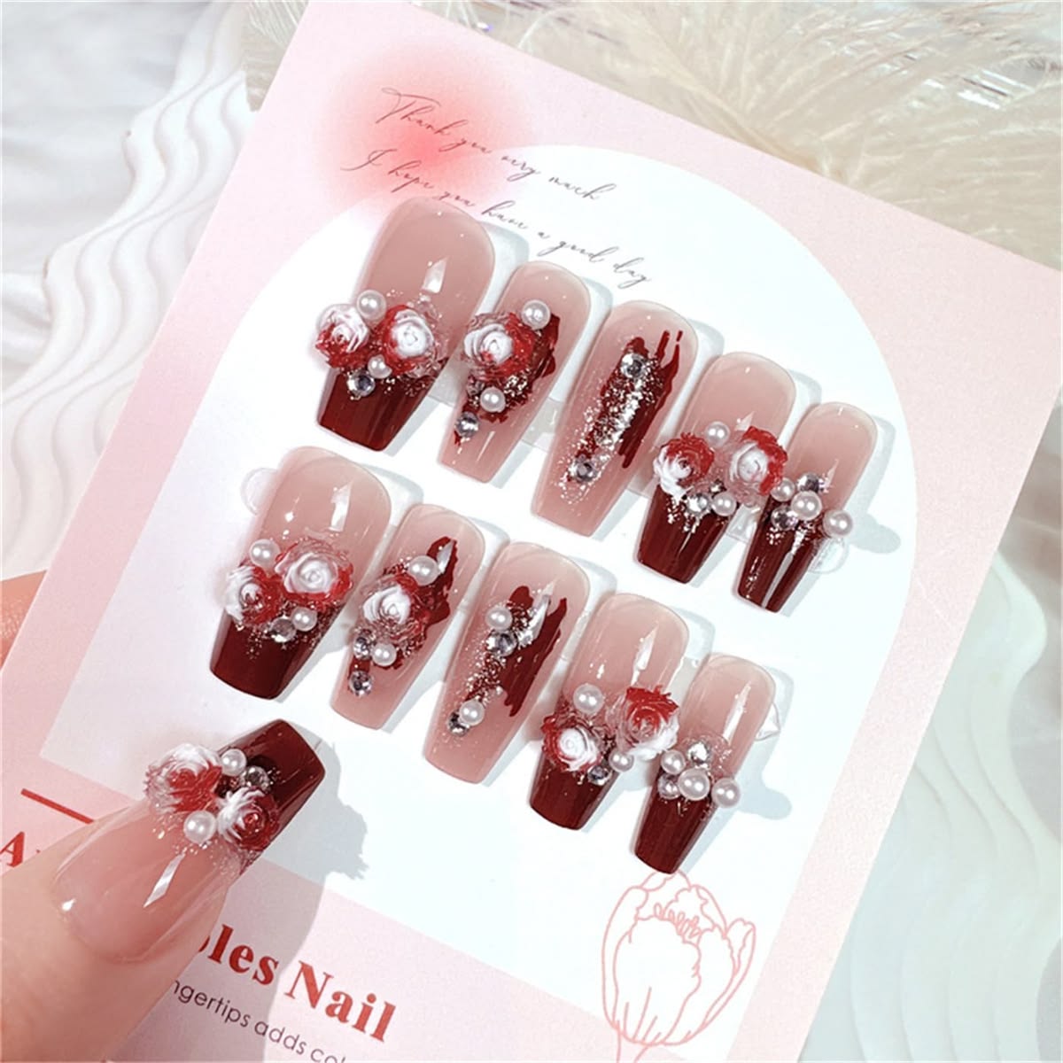 nude and red false nails featuring 3D white and red bloody rose charms, white pearls and clear diamantes, displayed on a floral backing card.