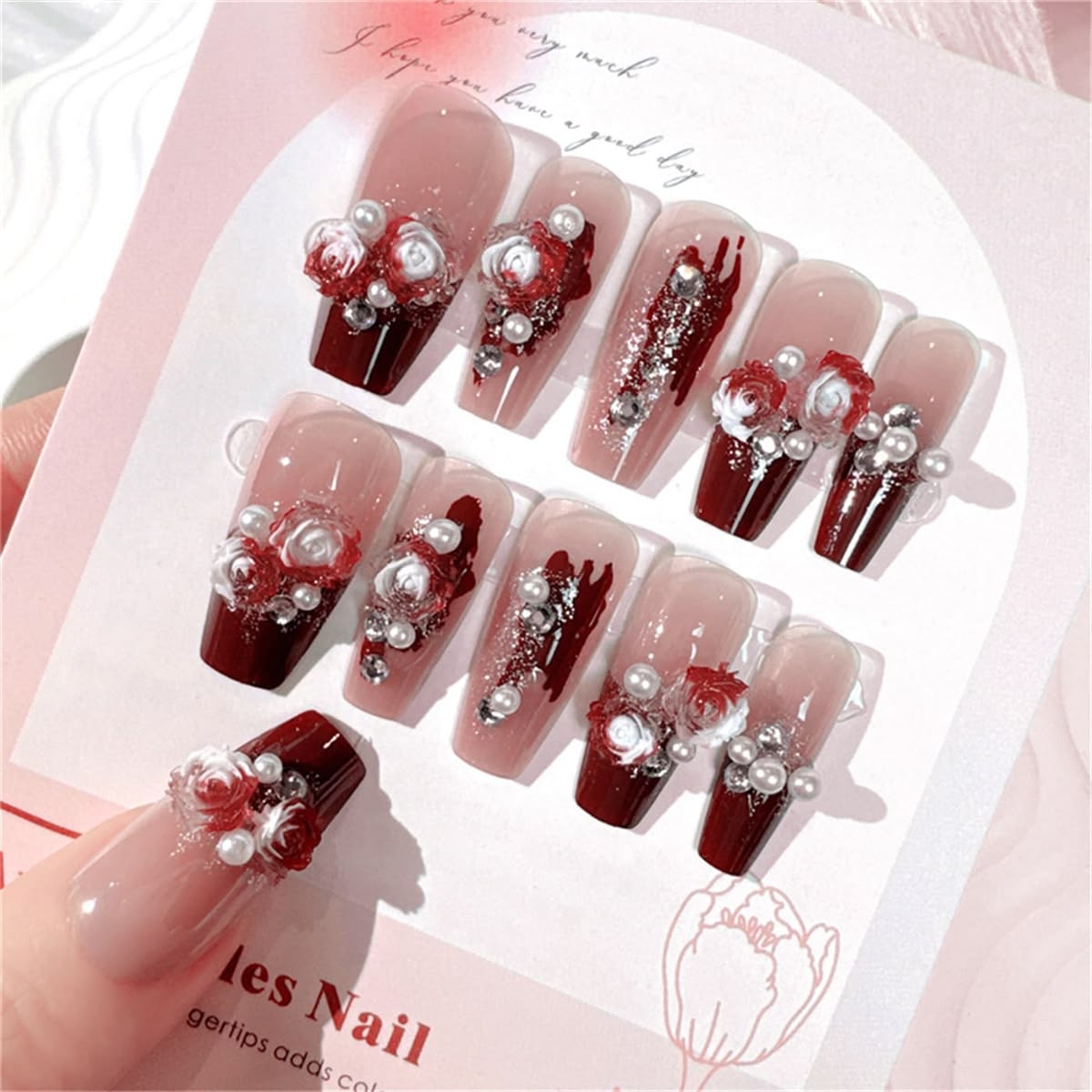 nude and red false nails featuring 3D white and red bloody rose charms, white pearls and clear diamantes, displayed on a floral backing card.