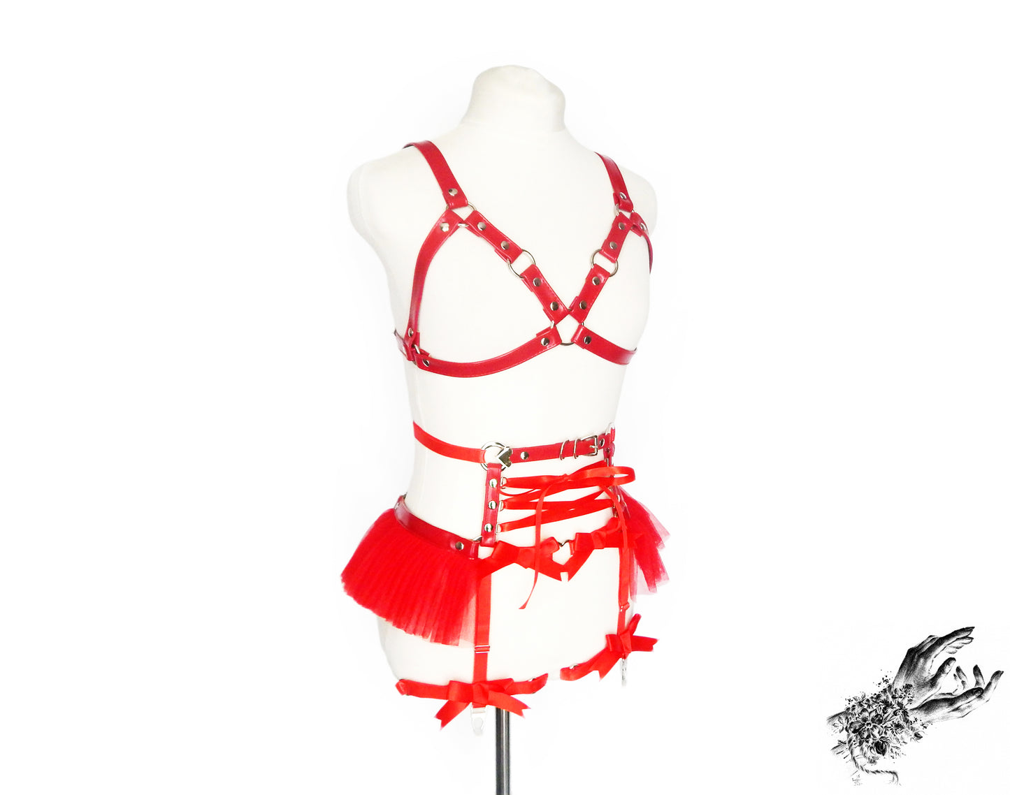 Red vegan leather harness set featuring a separate harness bra and garter belt with silver O ring hardware, red ruffled tulle and corset lacing at the waist, displayed on a mannequin against a white background.