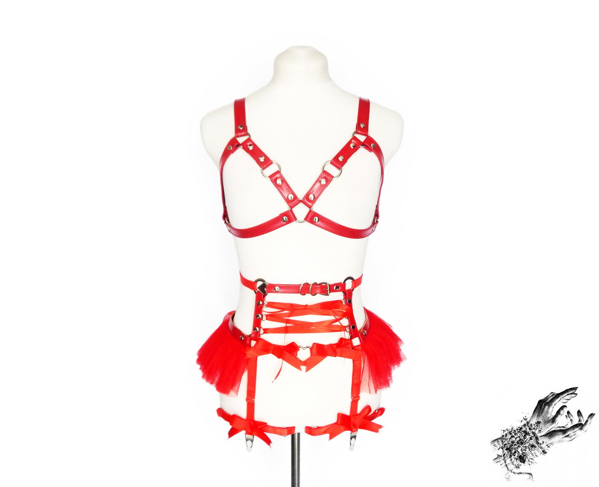 Front view of a red vegan leather harness set featuring a separate harness bra and garter belt with silver O ring hardware, red ruffled tulle and corset lacing at the waist, displayed on a mannequin against a white background.