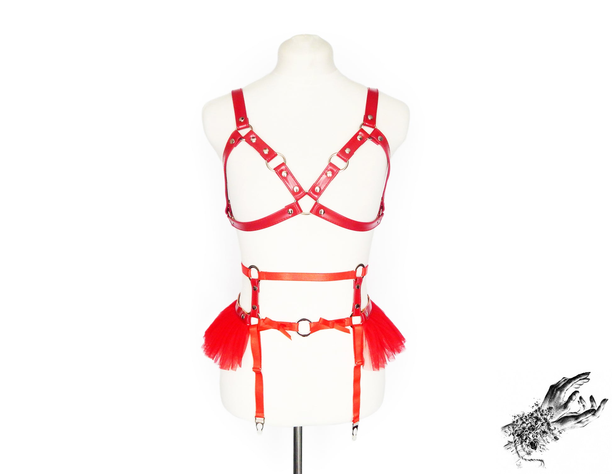 Front view of a red vegan leather harness set featuring a separate harness bra and garter belt with silver O ring hardware, red ruffled tulle accents and bow appliques at the waist, displayed on a mannequin against a white background.