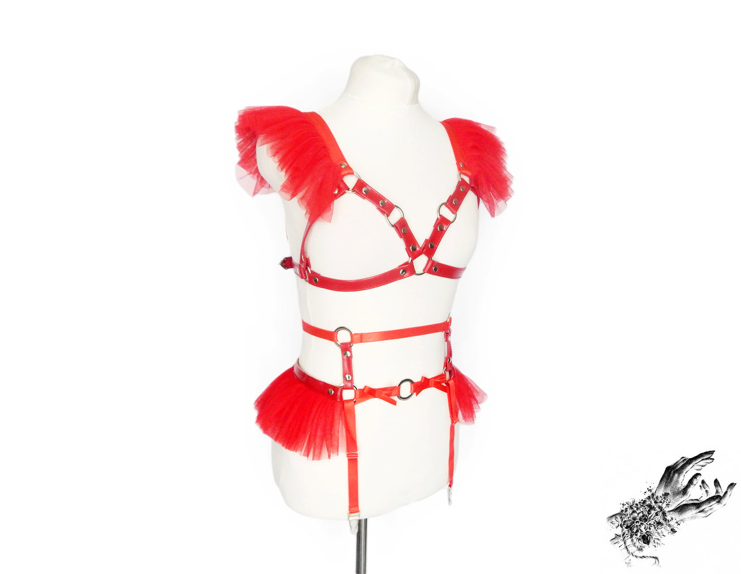 Red vegan leather harness set featuring a separate harness bra and garter belt with red ruffled tulle accents at the shoulders and waist and silver O ring hardware, displayed on a mannequin against a white background.