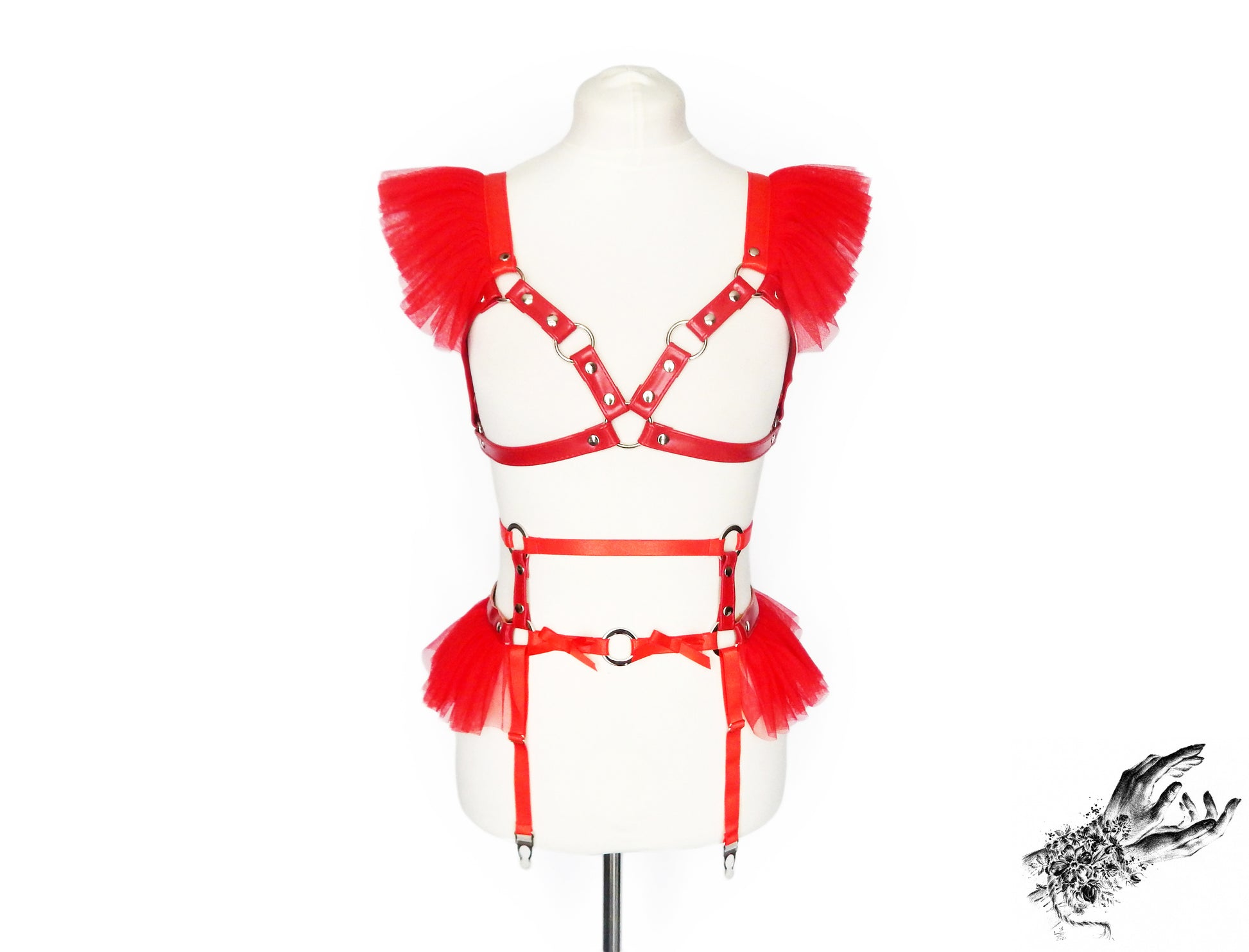 Front view of a red vegan leather harness set featuring a separate harness bra and garter belt with red ruffled tulle accents at the shoulders and waist and silver O ring hardware, displayed on a mannequin against a white background.