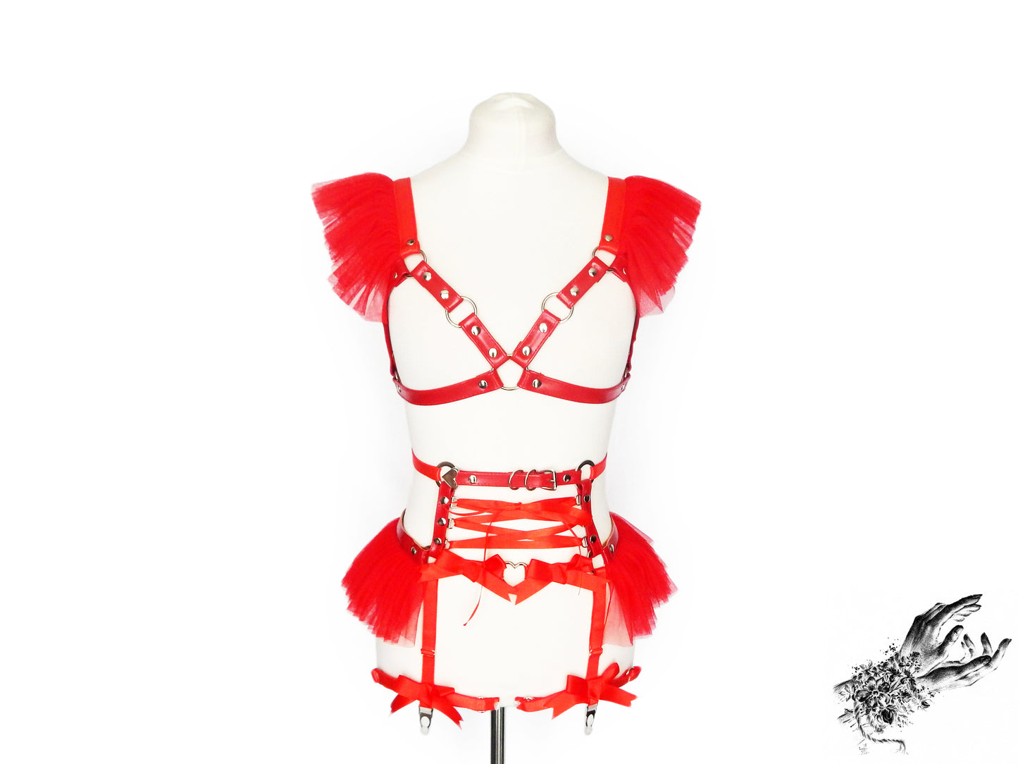 Front view of a red vegan leather harness set featuring a separate harness bra and garter belt with silver hardware, red ruffled tulle at the shoulders and waist and red ribbon corset lacing, displayed on a mannequin against a white background.
