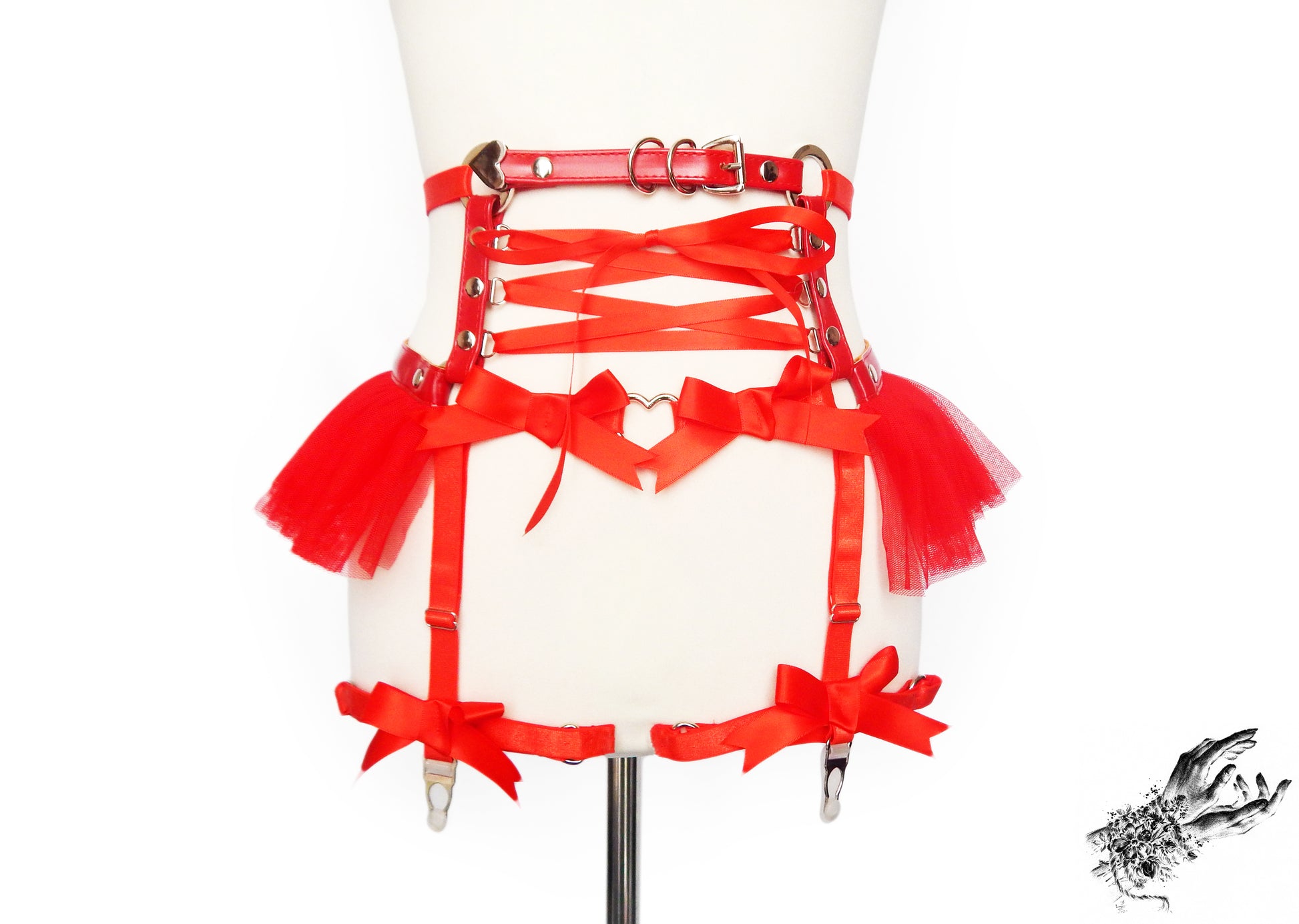 Red faux leather garter belt featuring ruffle tulle, corset lacing and bow appliques with silver hardware, displayed on a mannequin against a white background.