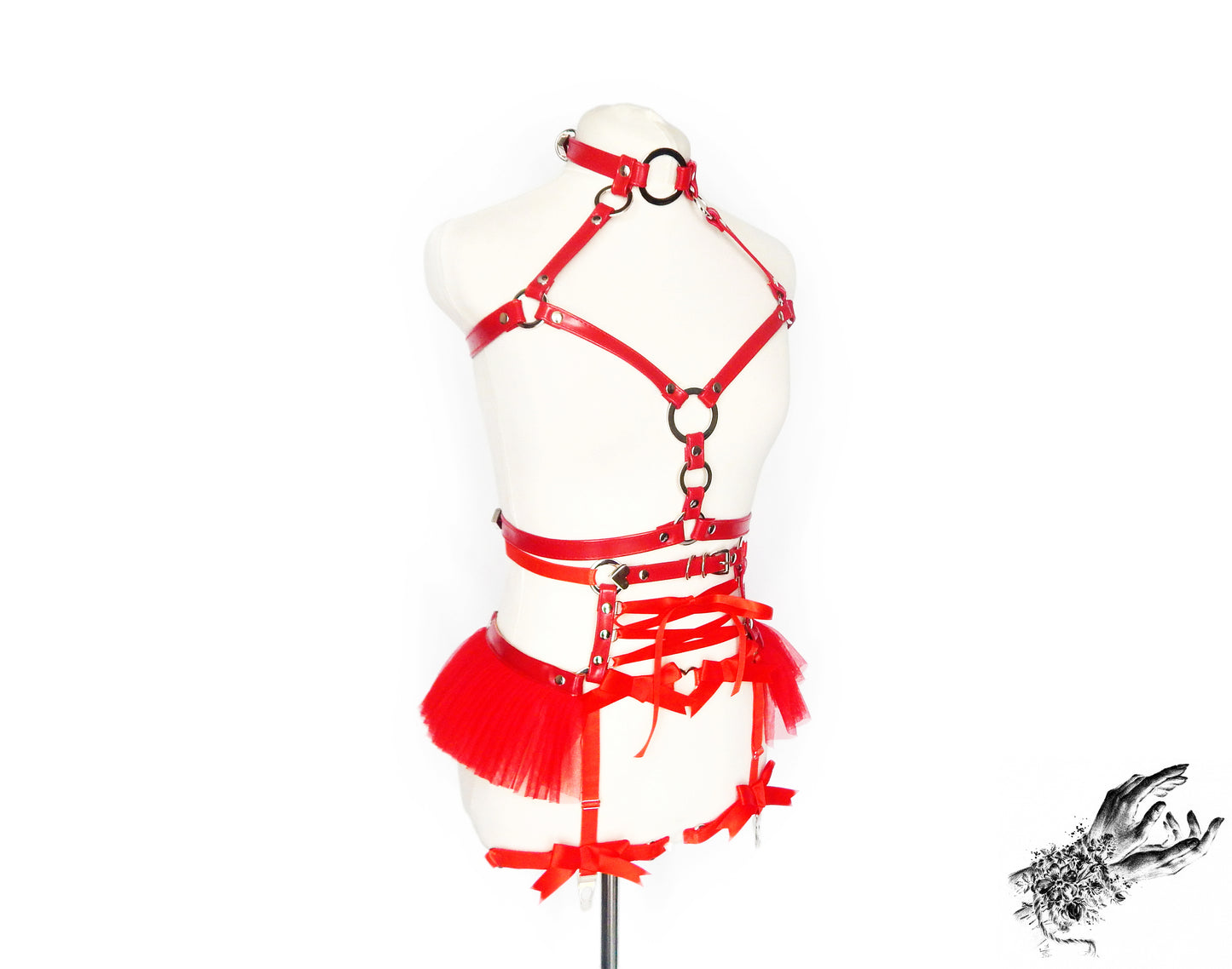 Red vegan leather harness set featuring a separate chest harness and garter belt with silver O ring hardware, red ruffled tulle accents and corset lacing at the waist, displayed on a mannequin against a white background.