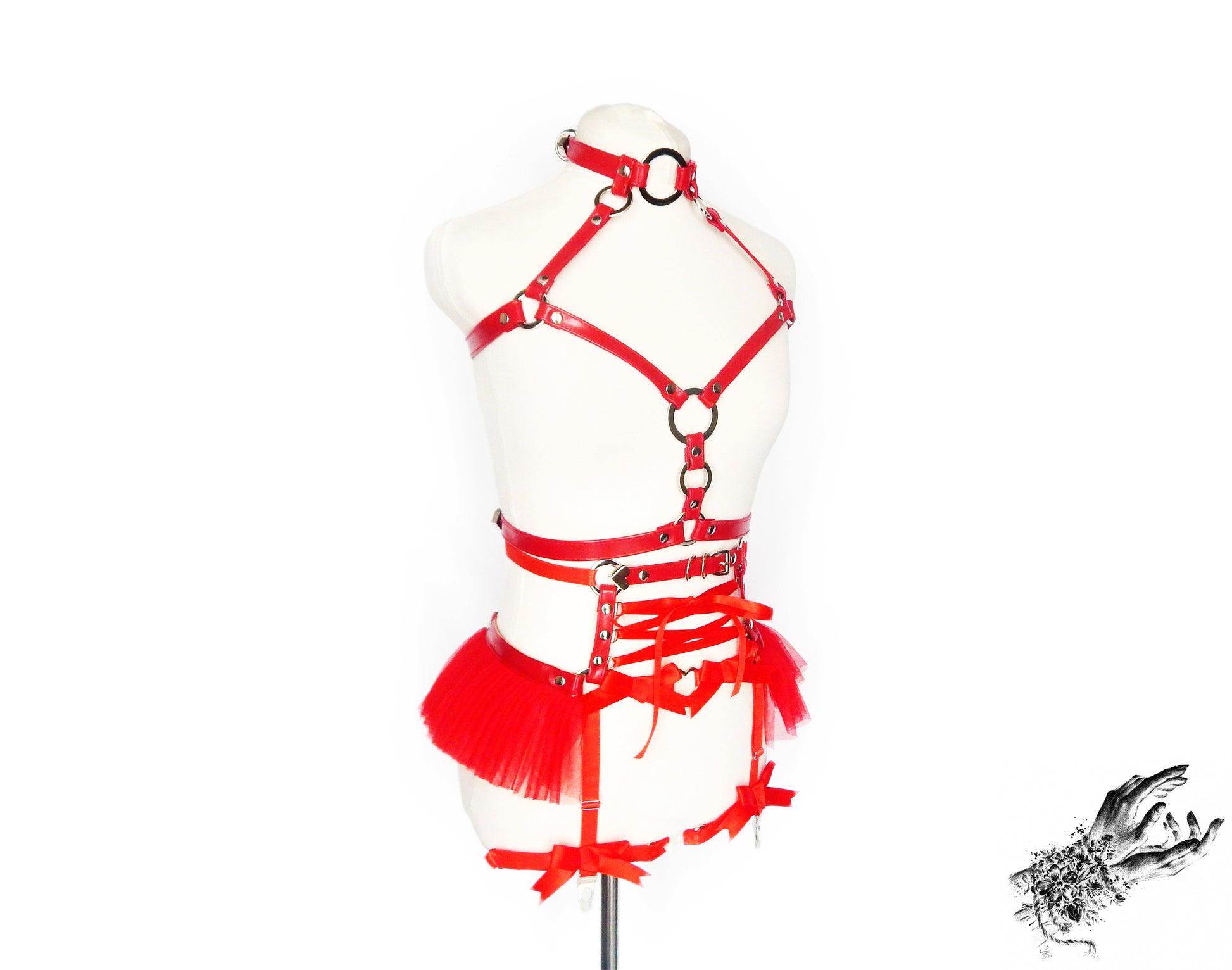 Red vegan leather harness set featuring a separate chest harness and garter belt with silver O ring hardware, red ruffled tulle accents and corset lacing at the waist, displayed on a mannequin against a white background.