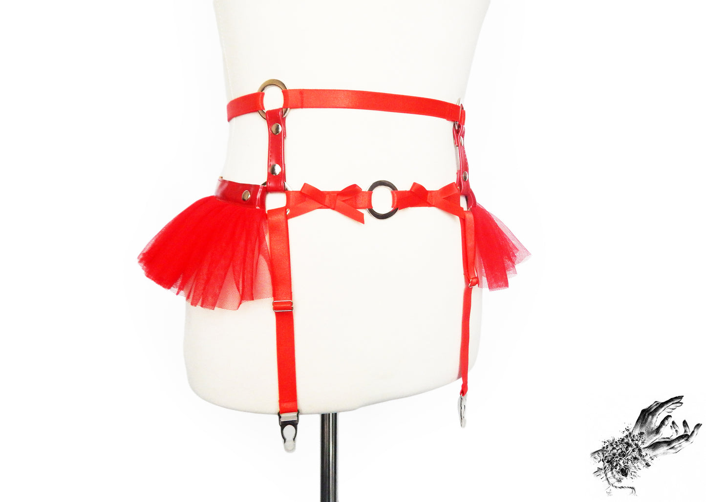 Red faux leather garter belt featuring silver O ring hardware, red ruffled tulle accents and bow appliques at the waist, displayed on a mannequin against a white background.