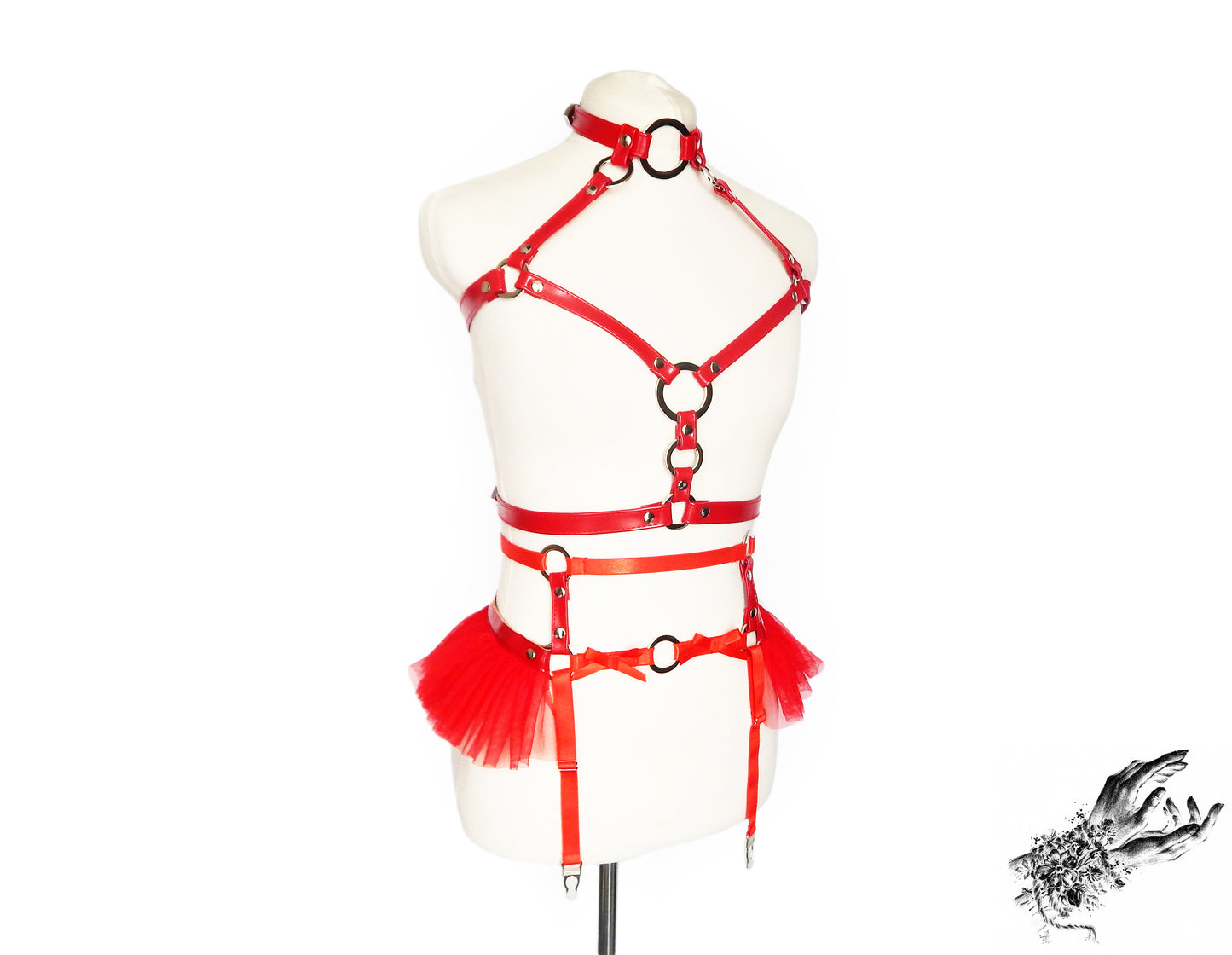 Red vegan leather harness set featuring a separate chest harness and garter belt with silver O ring hardware and red ruffled tulle accents at the hips, displayed on a mannequin against a white background.