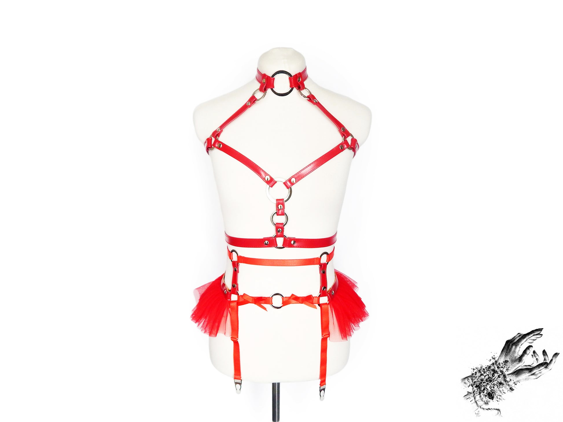 Front view of a red vegan leather harness set featuring a separate chest harness and garter belt with silver O ring hardware and red ruffled tulle accents at the hips, displayed on a mannequin against a white background.
