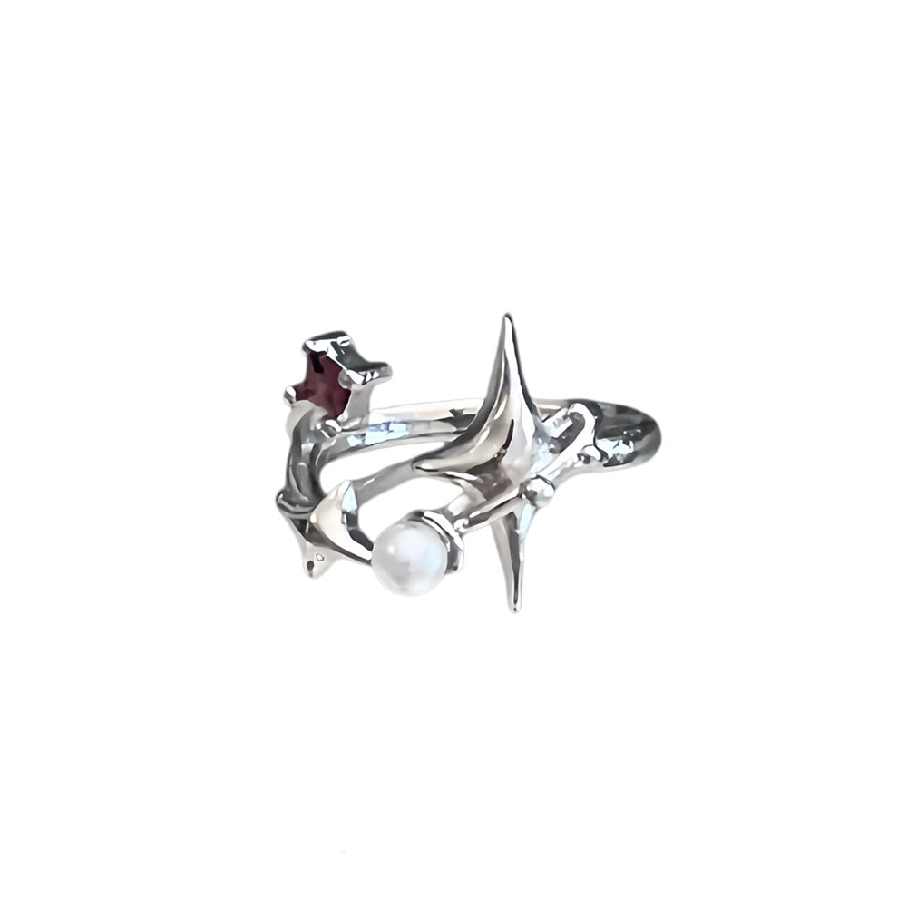A silver-toned ring featuring a stylized starburst design with a white pearl and a small dark red accent stone, shown on a plain white background.
