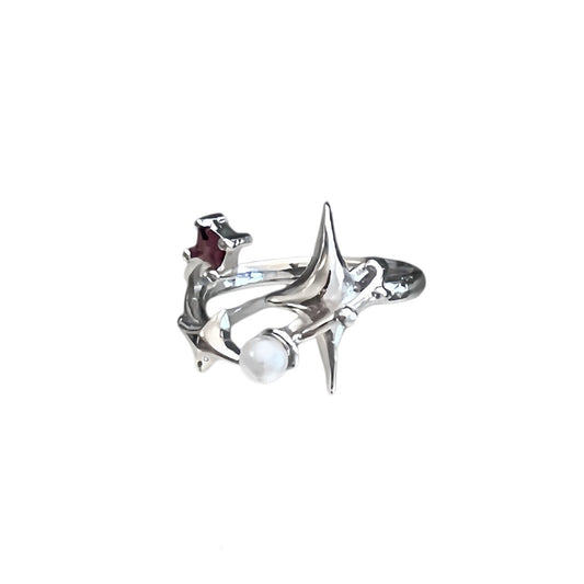 A silver-toned ring featuring a stylized starburst design with a white pearl and a small dark red accent stone, shown on a plain white background.