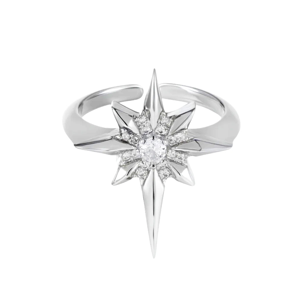 A silver-toned starburst ring featuring a central round clear gemstone surrounded by smaller clear stones, with sharp pointed rays extending downward and outward, shown on a plain white background.