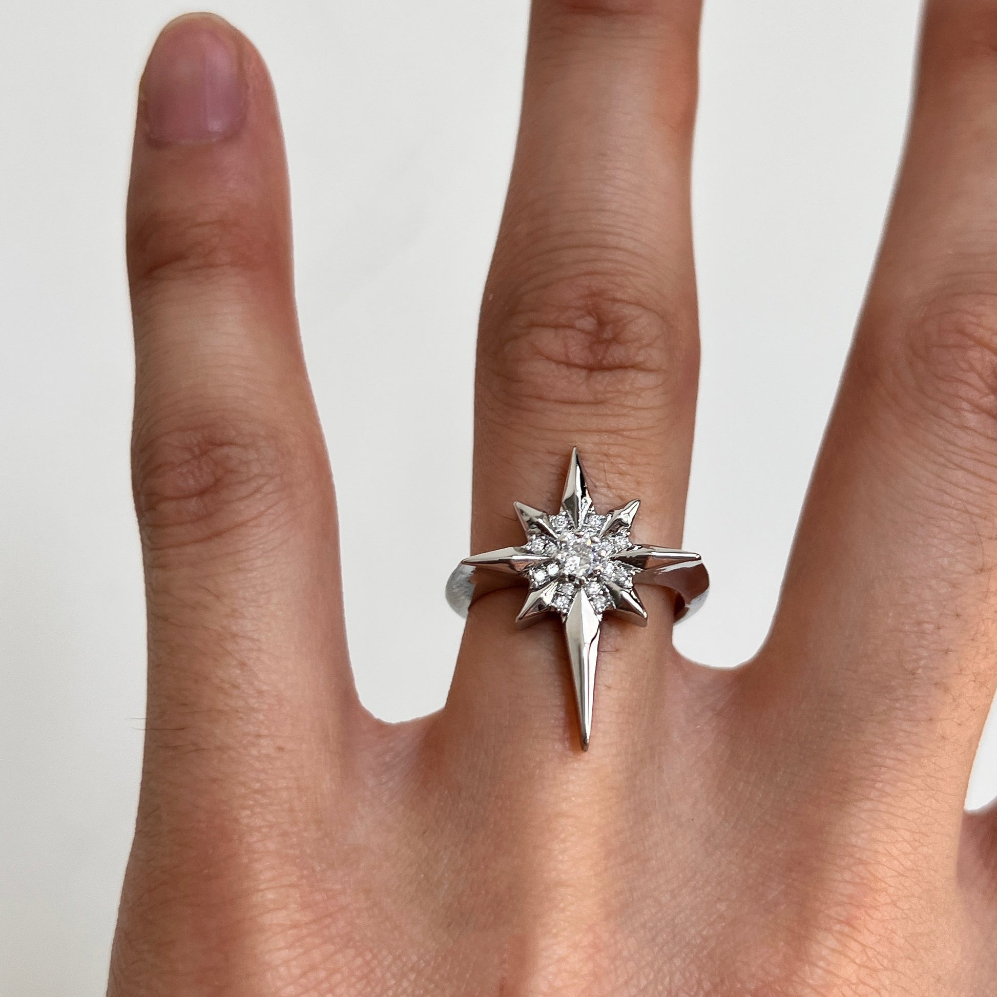 A silver-toned starburst ring with clear gemstones, shown worn on a person's ring finger against a plain light background.