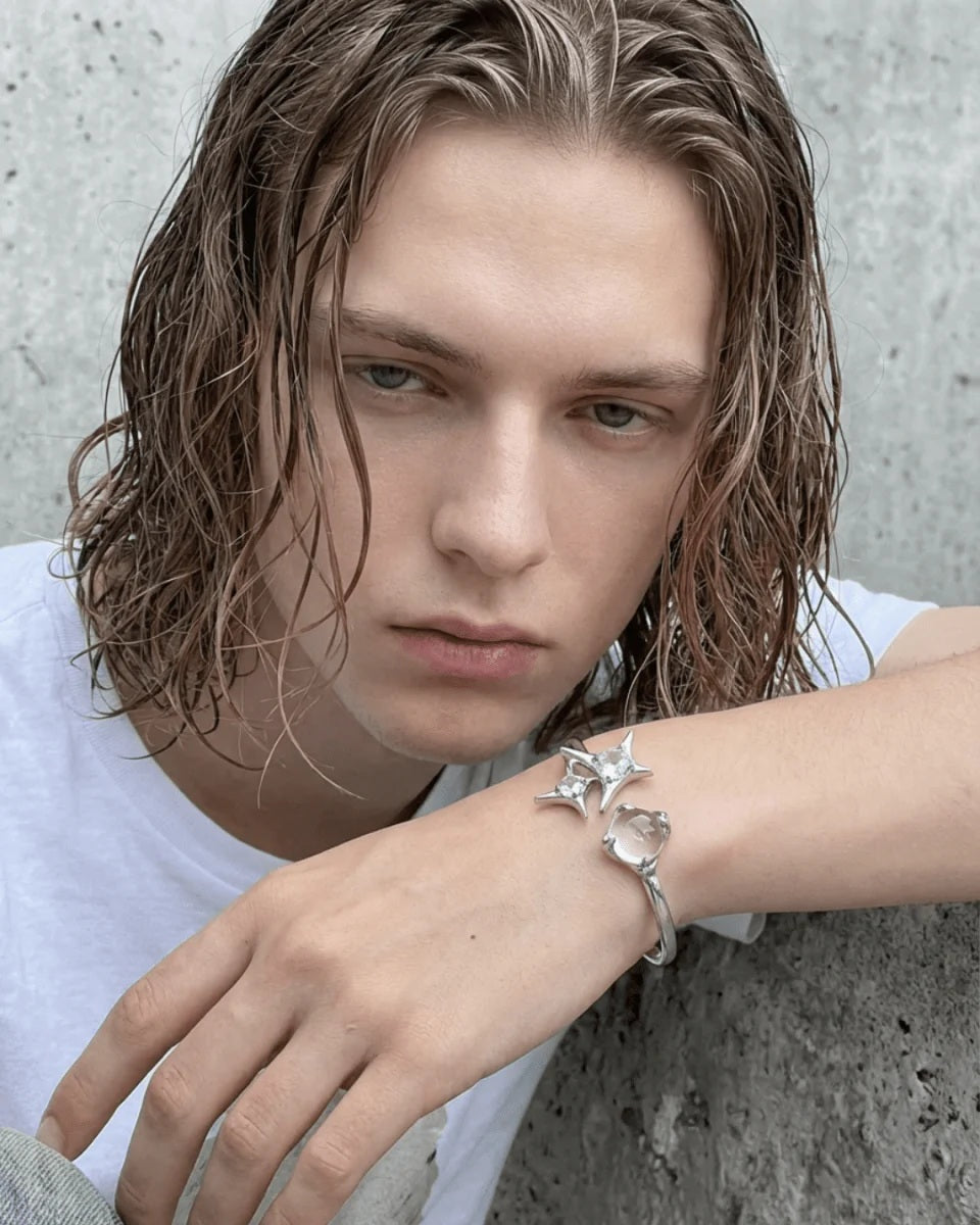 Modelled photo of a silver plated bangle featuring a silver starburst design, wrap-around cuff and clear round glass crystal gemstones, styled with long, wet-look hair and a white t-shirt for an edgy street fashion style.