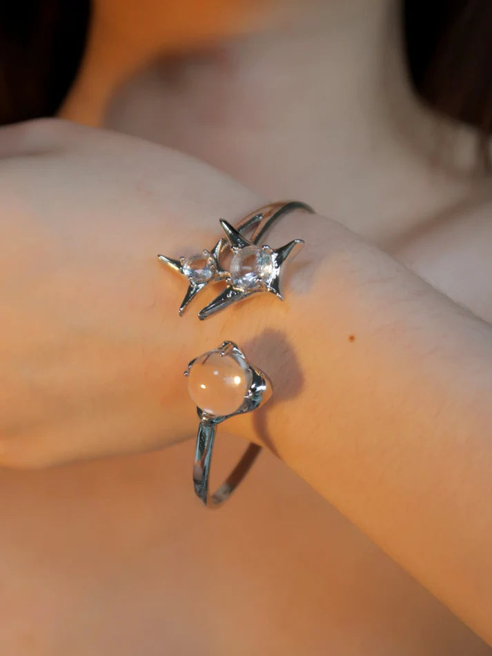 Modelled photo of a silver plated bangle featuring a silver starburst design, wrap-around cuff and clear round glass crystal gemstones, worn by a wrist in warm, sunset lighting.