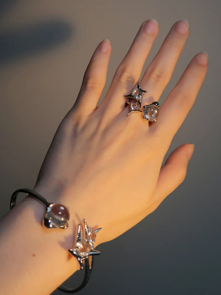 Worn photo of a silver plated bangle featuring a silver starburst design, wrap-around cuff and clear round glass crystal gemstones, styled with a matching ring in warm, sunset lighting.