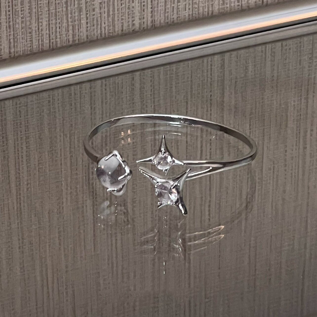 A silver plated bangle featuring a silver starburst design, wrap-around cuff and clear round glass crystal gemstones, displayed against a glossy wooden background.