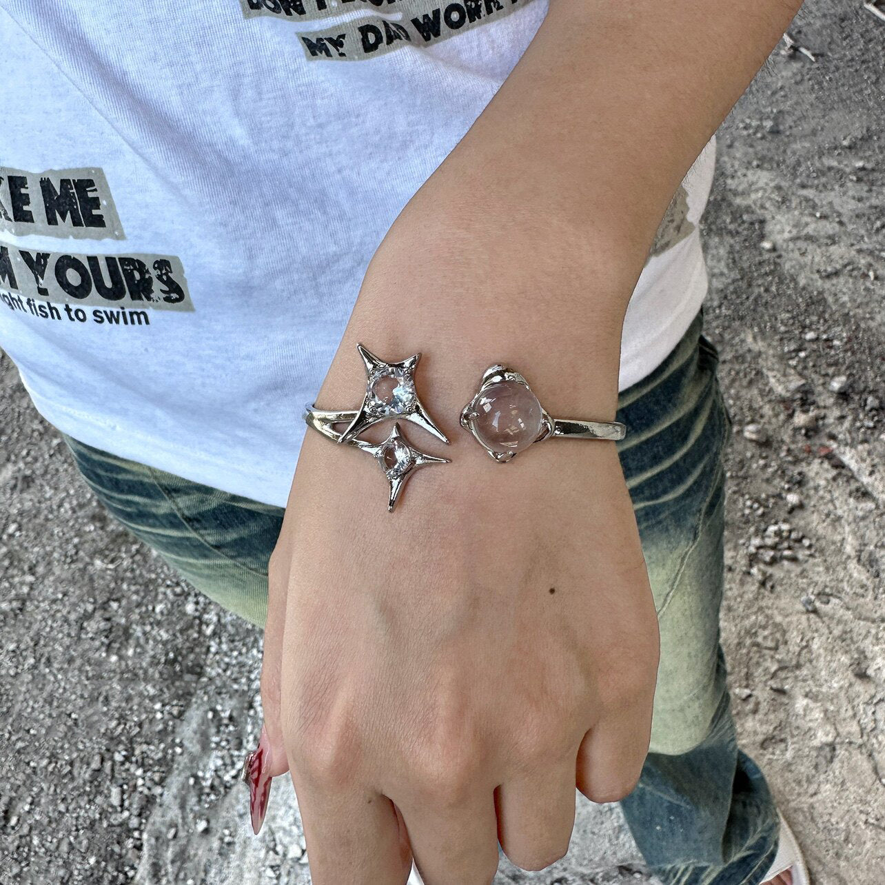 Worn photo of a silver plated costume jewellery bangle featuring a silver starburst design, wrap-around cuff and clear round glass crystal gemstones, styled with a white graphic t-shirt and faded denim jeans for a street fashion aesthetic.