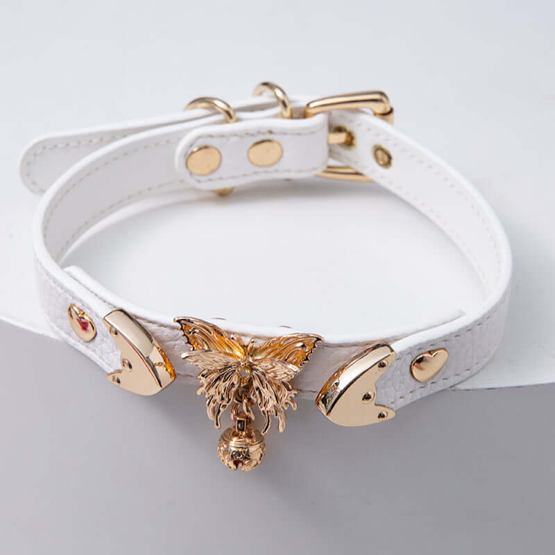 White leather choker featuring ornate gold butterfly and bell hardware and an adjustable gold tone buckle at the back, designed for pastel goth and fairy kei fashion in the UK