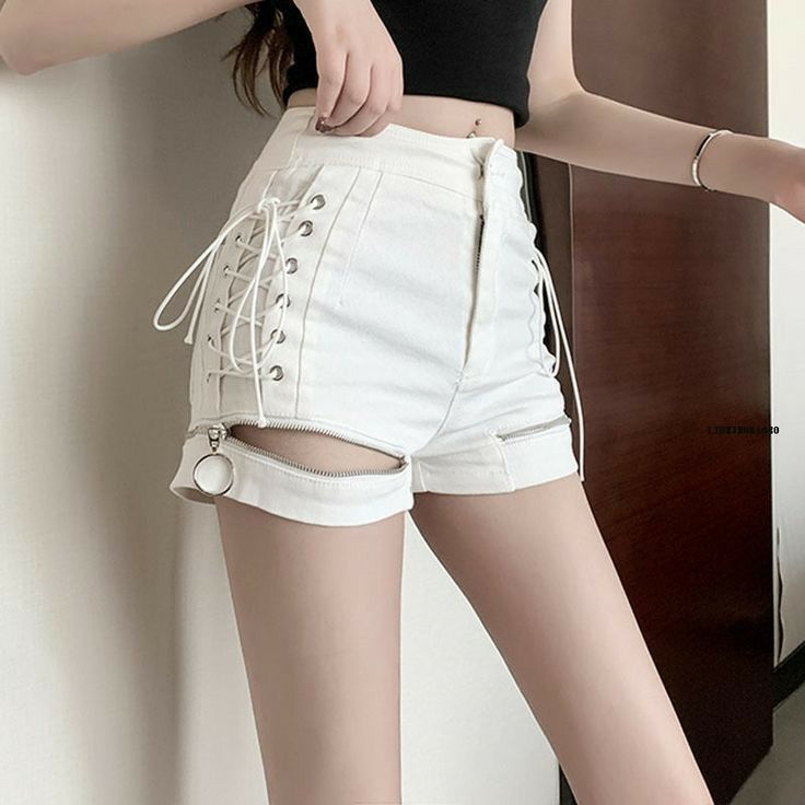 A person wearing white high-waisted shorts with lace-up side detailing, rolled cuffs, and a front zipper cutout, paired with a black cropped top in an indoor setting.