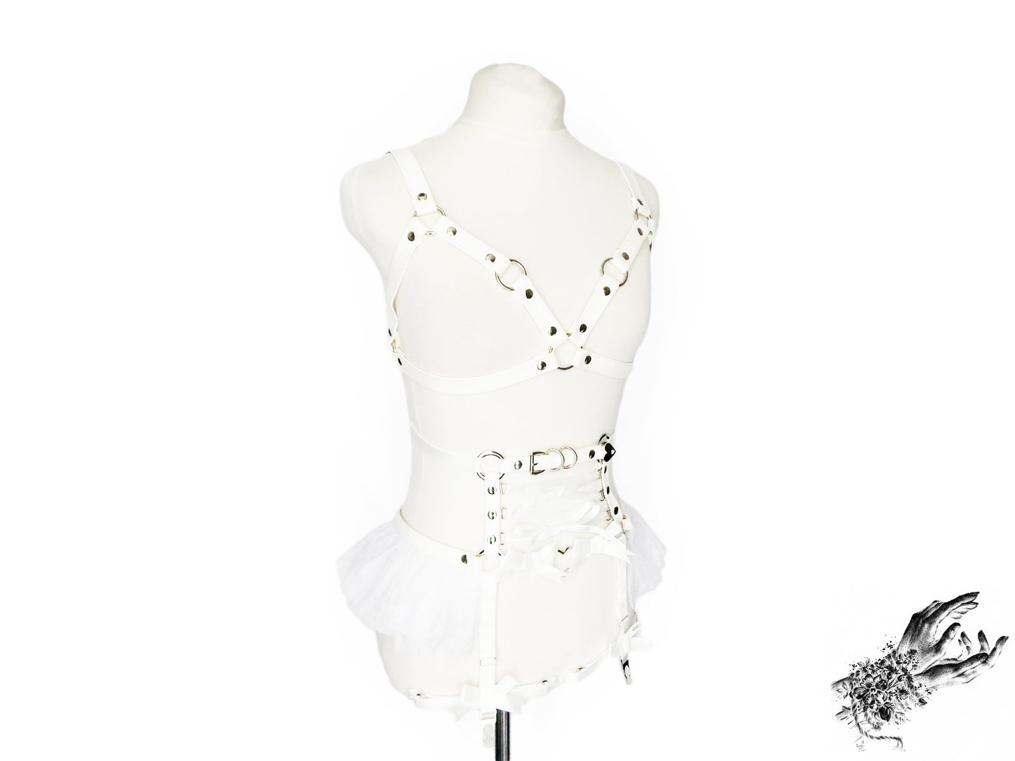 A white vegan leather harness set featuring a separate harness bra and garter belt with silver heart ring hardware, white ruffled tulle accents and corset lacing at the waist, displayed on a mannequin against a white background.