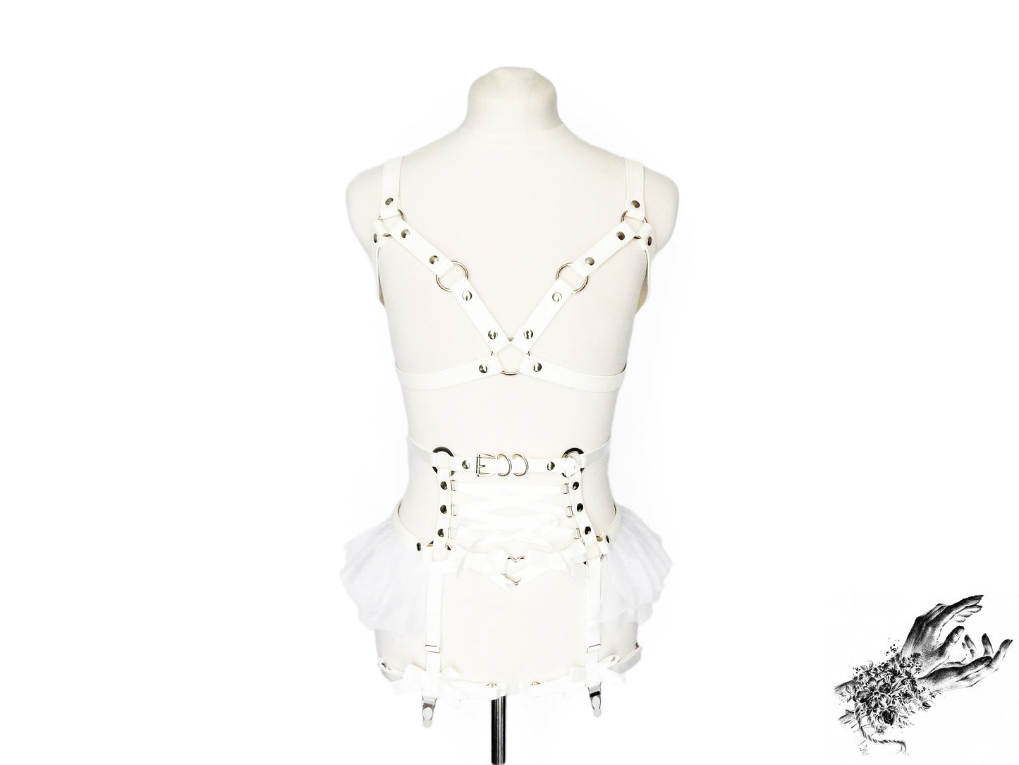 Front view of a white vegan leather harness set featuring a separate harness bra and garter belt with silver heart ring hardware, white ruffled tulle accents and corset lacing at the waist, displayed on a mannequin against a white background.