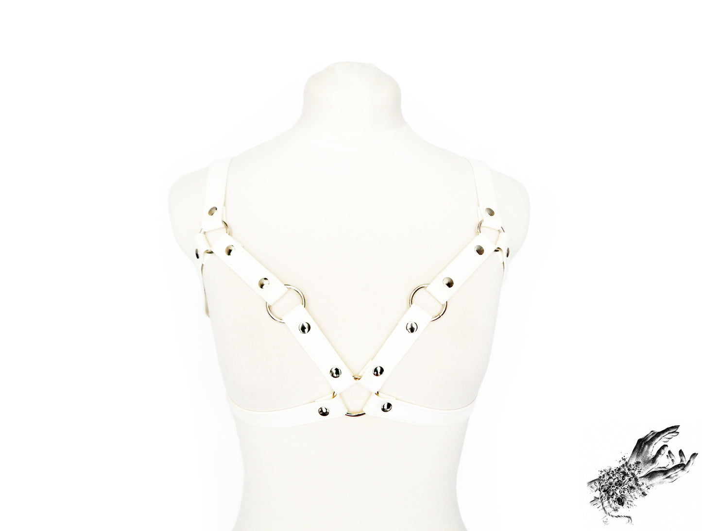 White vegan leather harness bra featuring silver O ring hardware and adjustable elastic shoulder straps and faux leather buckled underbust strap, displayed on a mannequin against a white background.
