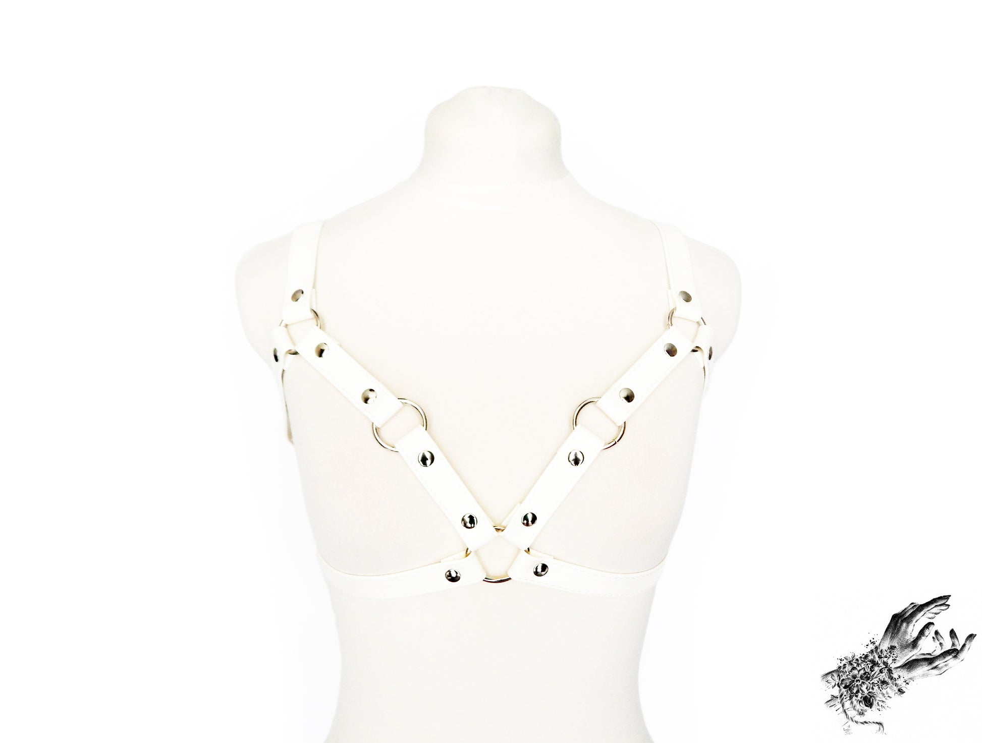 White vegan leather harness bra featuring silver O ring hardware and adjustable elastic shoulder straps and faux leather buckled underbust strap, displayed on a mannequin against a white background.