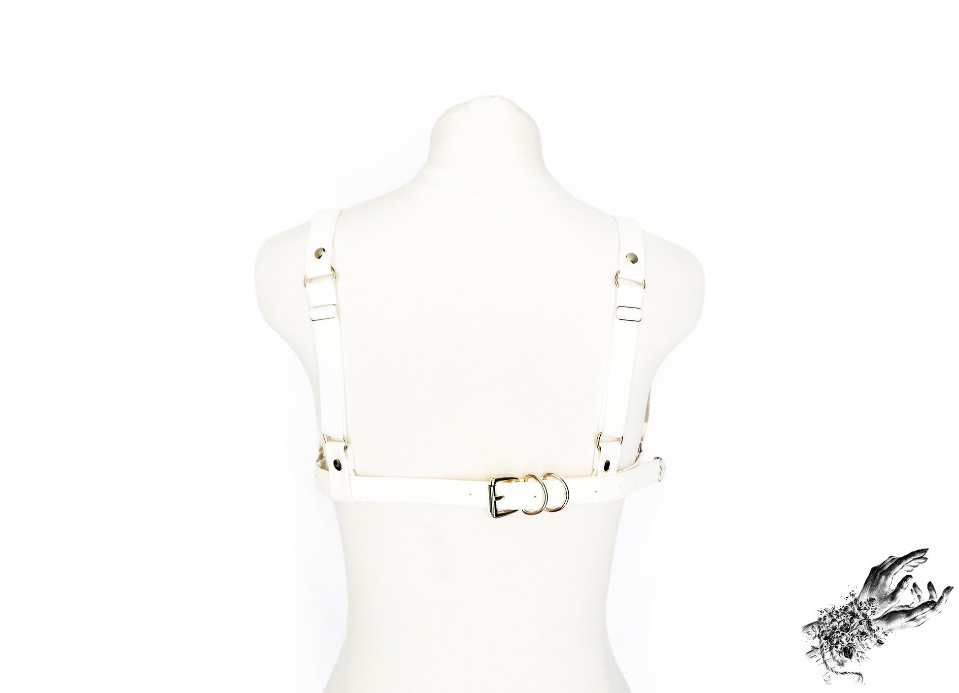 Rear view of a white vegan leather harness bra featuring silver hardware, adjustable elastic shoulder straps and buckled faux leather underbust strap, displayed on a mannequin against a white background.