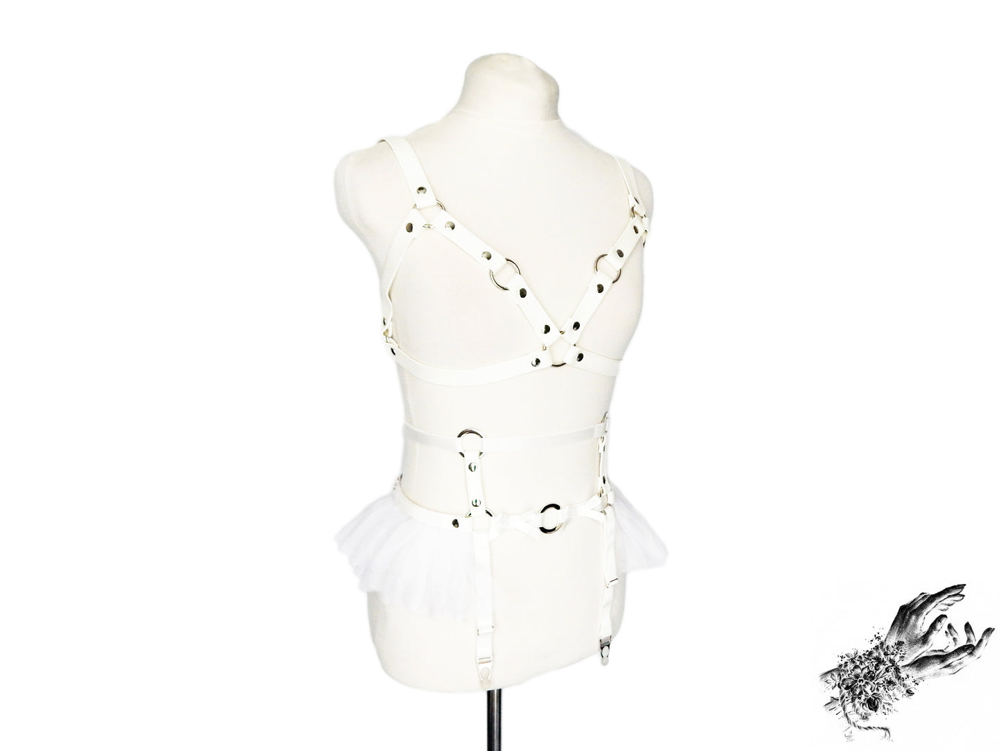 White vegan leather harness set featuring a separate harness bra and garter belt with silver O ring hardware, white ruffled tulle accents and bow appliques at the waist, displayed on a mannequin against a white background.