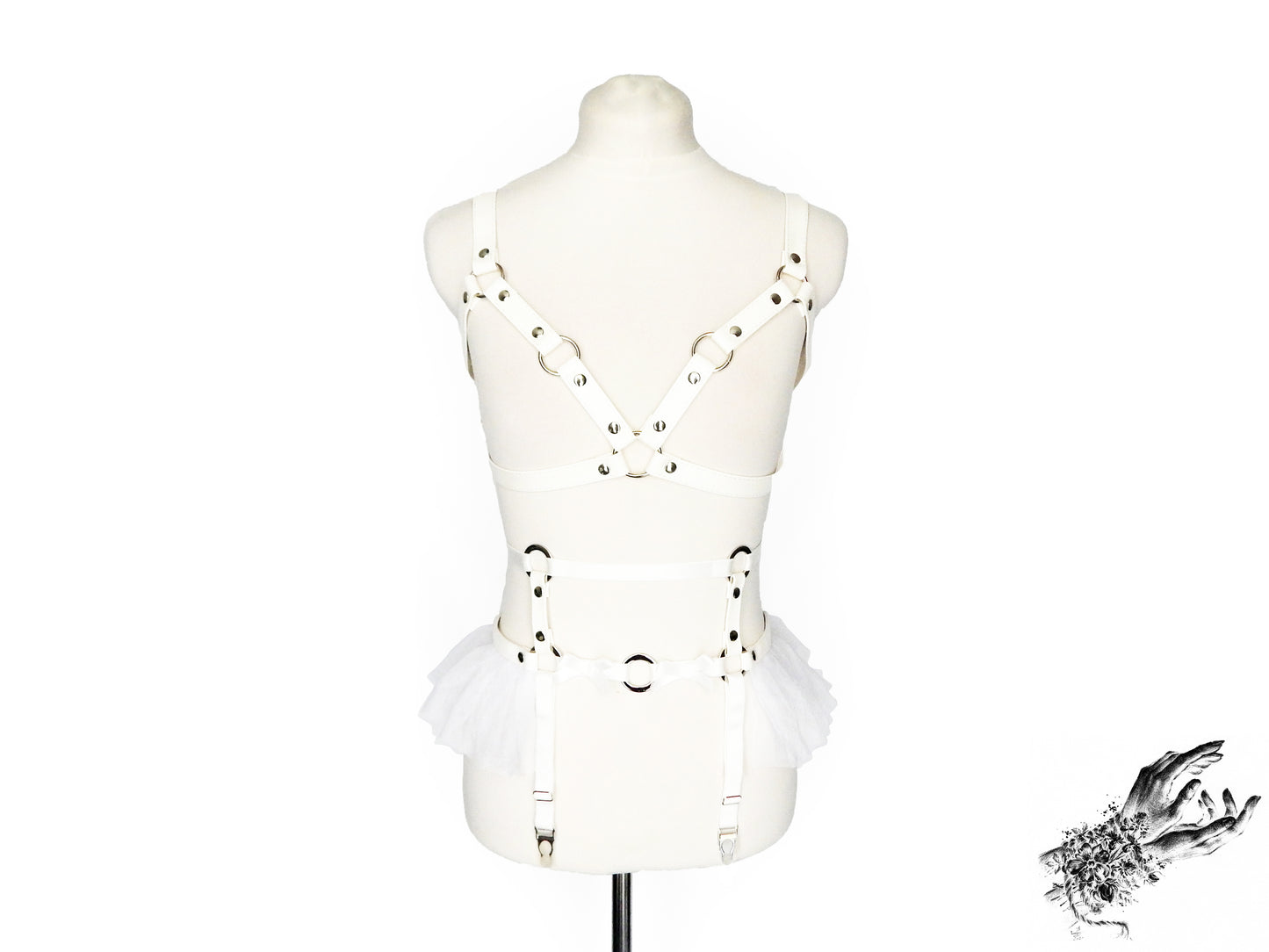 Front view of a white vegan leather harness set featuring a separate harness bra and garter belt with silver O ring hardware, white ruffled tulle accents and bow appliques at the waist, displayed on a mannequin against a white background.