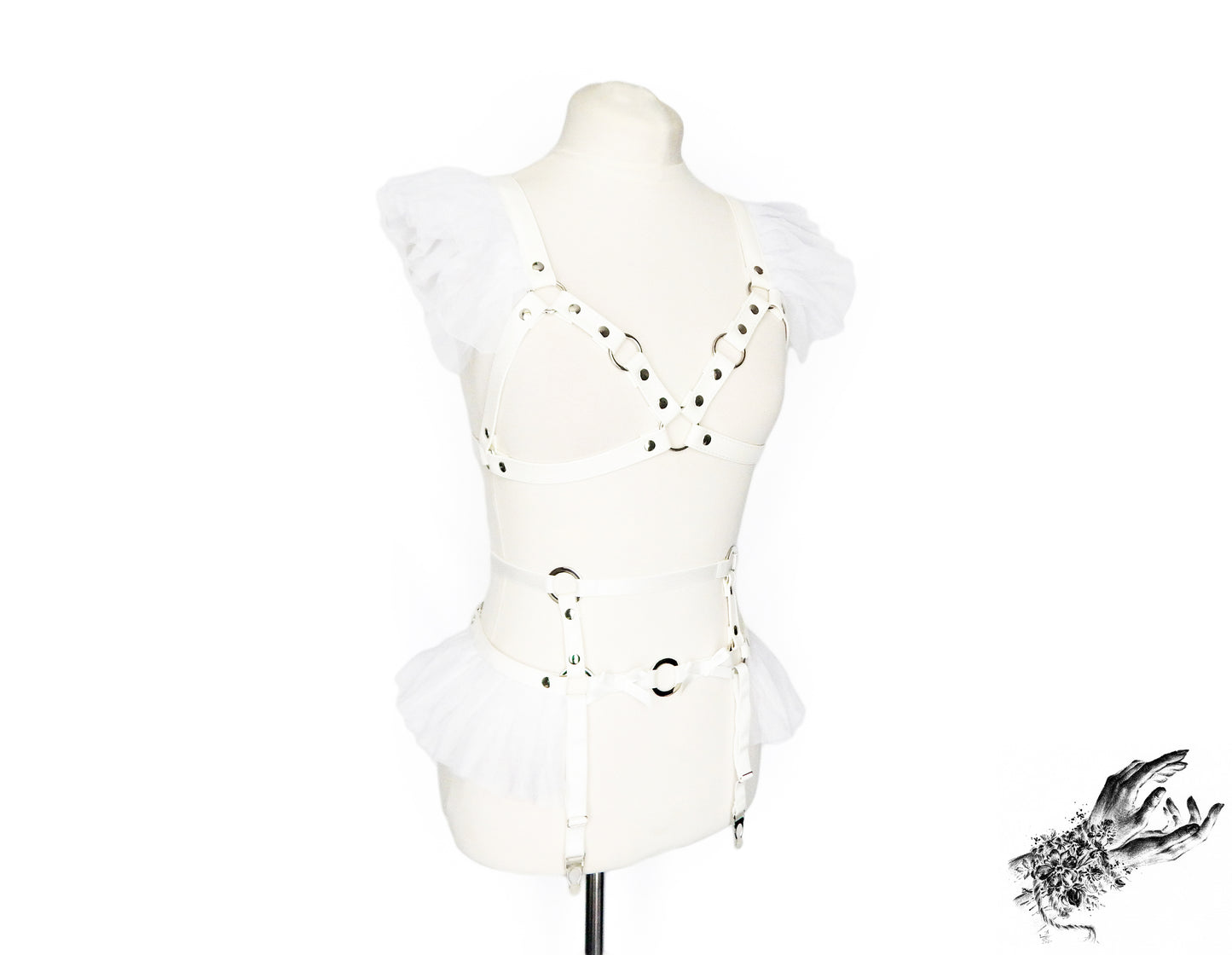 White faux leather harness set featuring a separate harness bra and garter belt with white ruffled tulle accents at the shoulders and hips, bow appliques and silver O ring hardware, displayed on a mannequin against a white background.