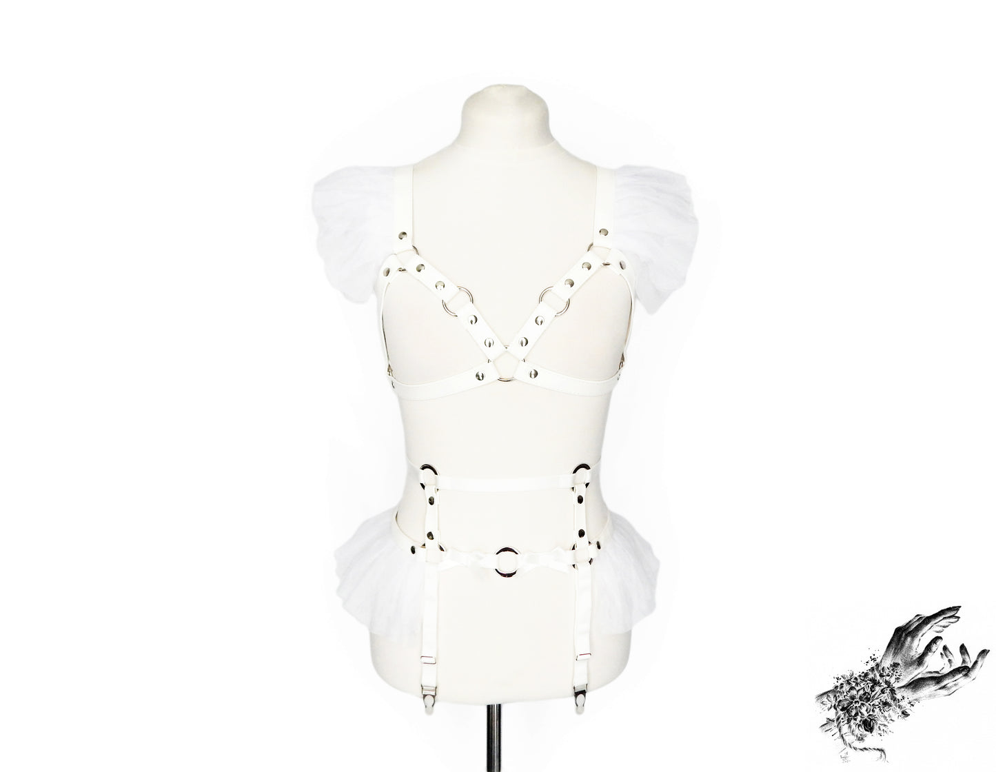 Front view of a white faux leather harness set featuring a separate harness bra and garter belt with white ruffled tulle accents at the shoulders and hips, bow appliques and silver O ring hardware, displayed on a mannequin against a white background.
