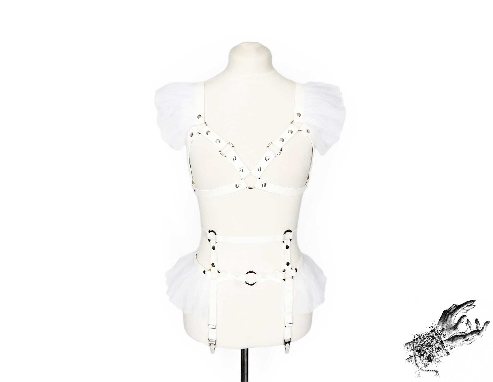 Front view of a white faux leather harness set featuring a separate harness bra and garter belt with white ruffled tulle accents at the shoulders and hips, bow appliques and silver O ring hardware, displayed on a mannequin against a white background.