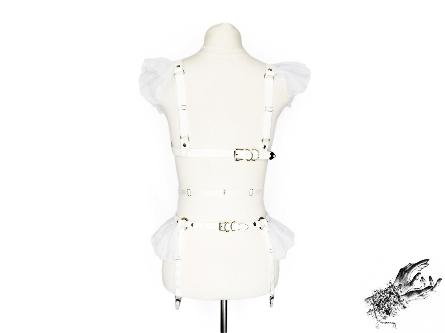 Rear view of a white faux leather harness set showing the white ruffled tulle accents at the shoulders and hips, adjustable elastic shoulder and suspender straps and buckled faux leather chest and hip straps, displayed on a mannequin against a white background.