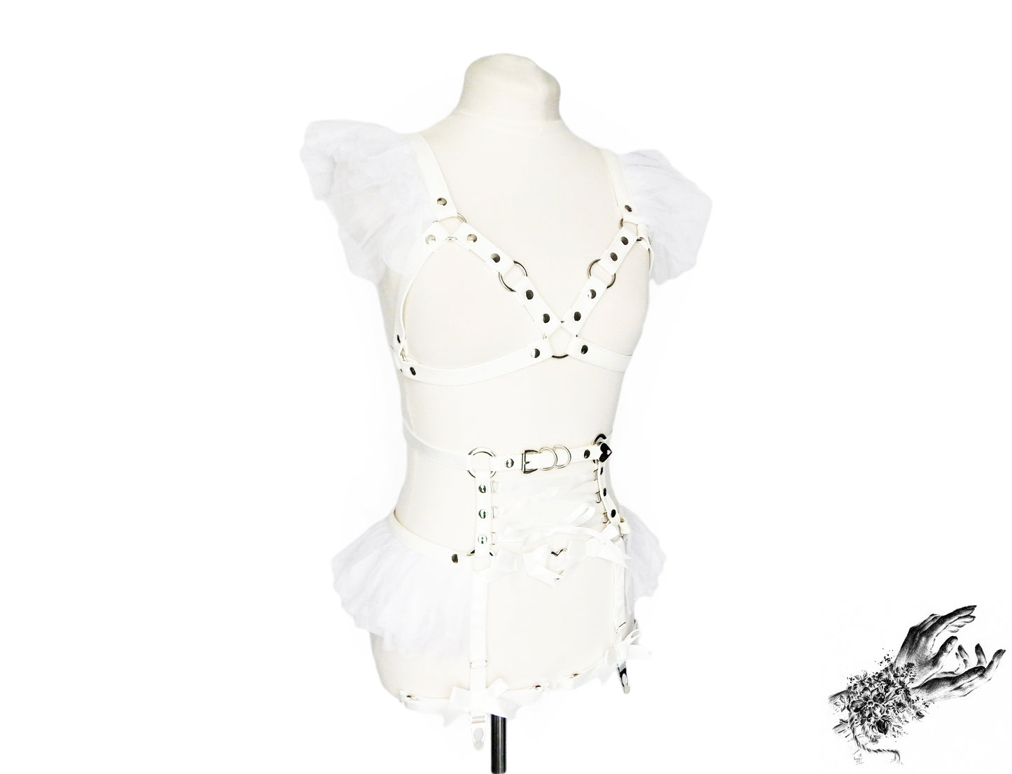 White vegan leather harness set featuring a separate harness bra and garter belt with white ruffled tulle accents at the shoulders and hips, corset lacing and silver heart ring hardware, displayed on a mannequin against a white background.