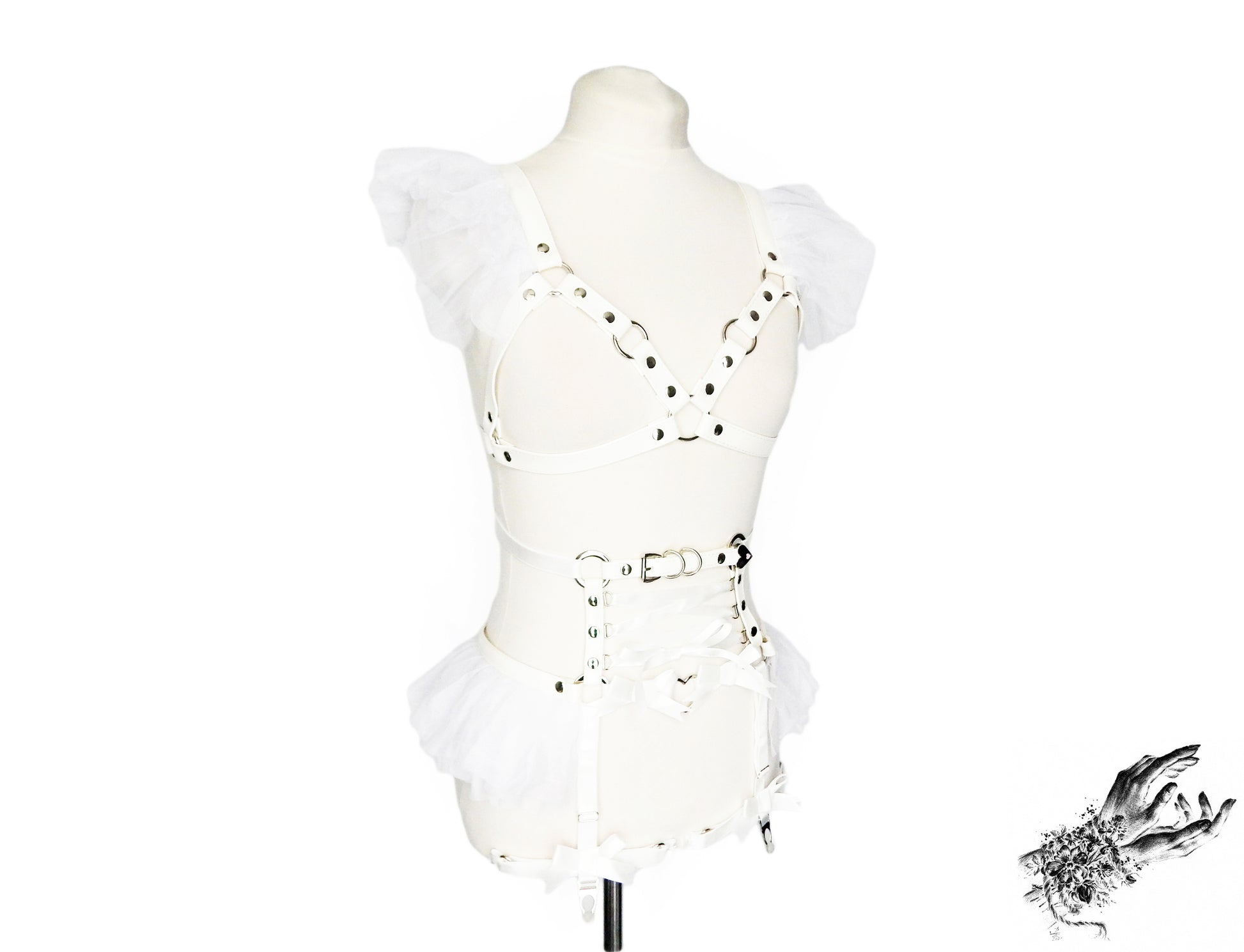 White vegan leather harness set featuring a separate harness bra and garter belt with white ruffled tulle accents at the shoulders and hips, corset lacing and silver heart ring hardware, displayed on a mannequin against a white background.