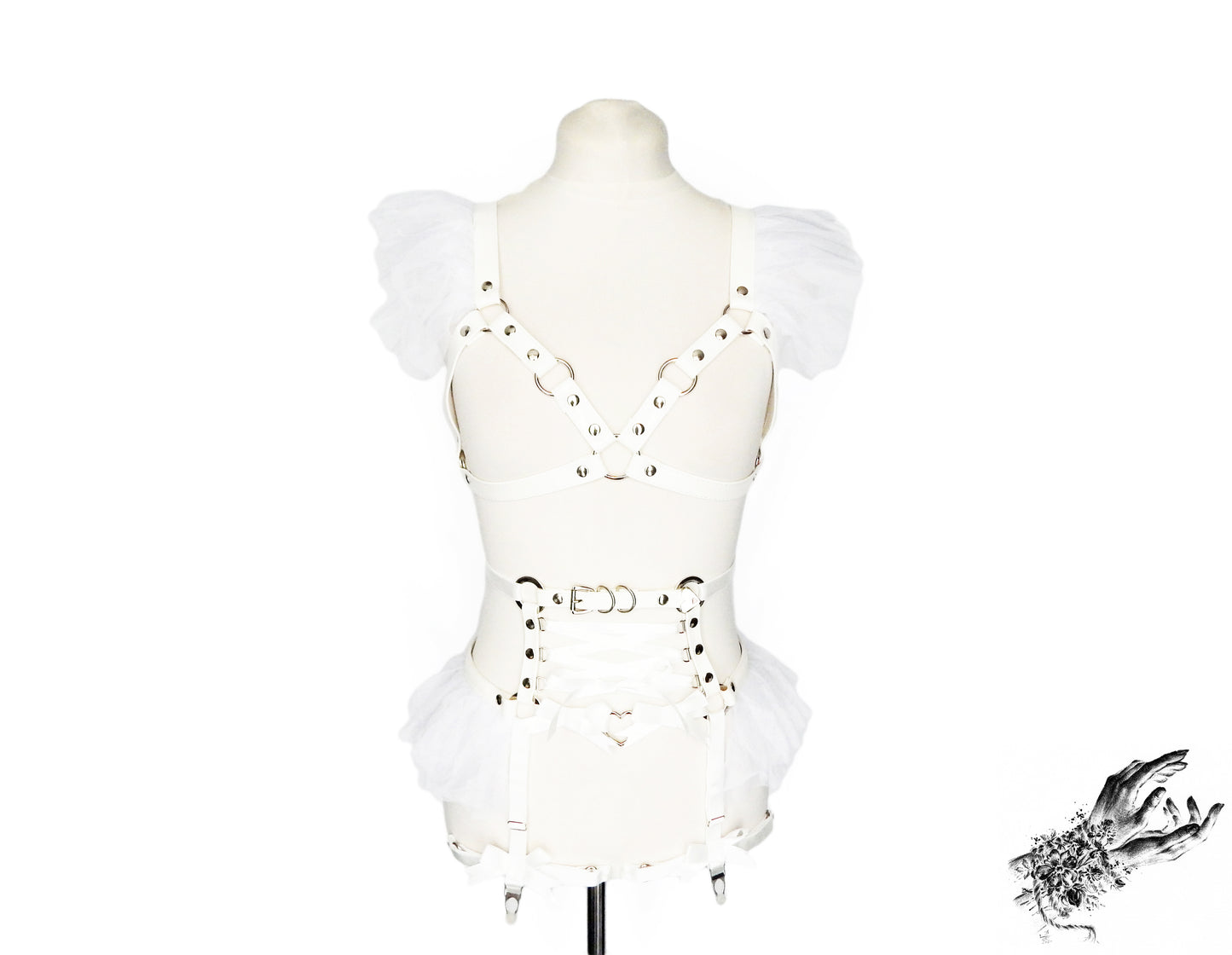 Front view of a white vegan leather harness set featuring a separate harness bra and garter belt with white ruffled tulle accents at the shoulders and hips, corset lacing and silver heart ring hardware, displayed on a mannequin against a white background.