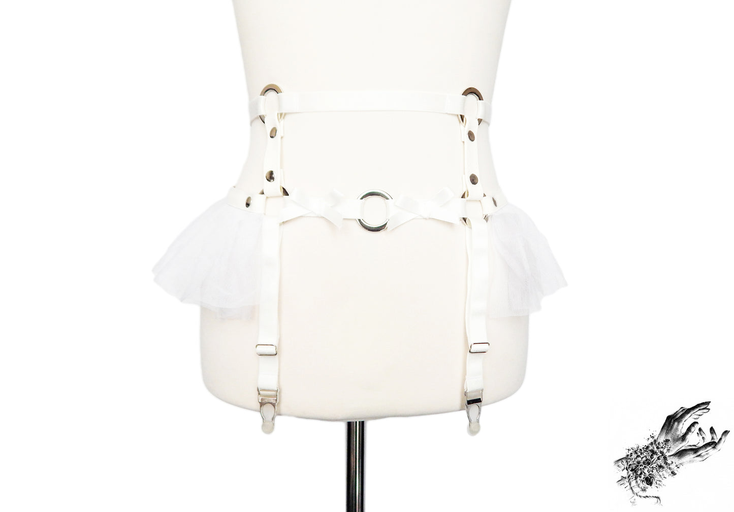 White faux leather garter belt featuring silver O ring hardware, white ruffled tulle and bow appliques at the waist with adjustable suspender straps, displayed on a mannequin against a white background.