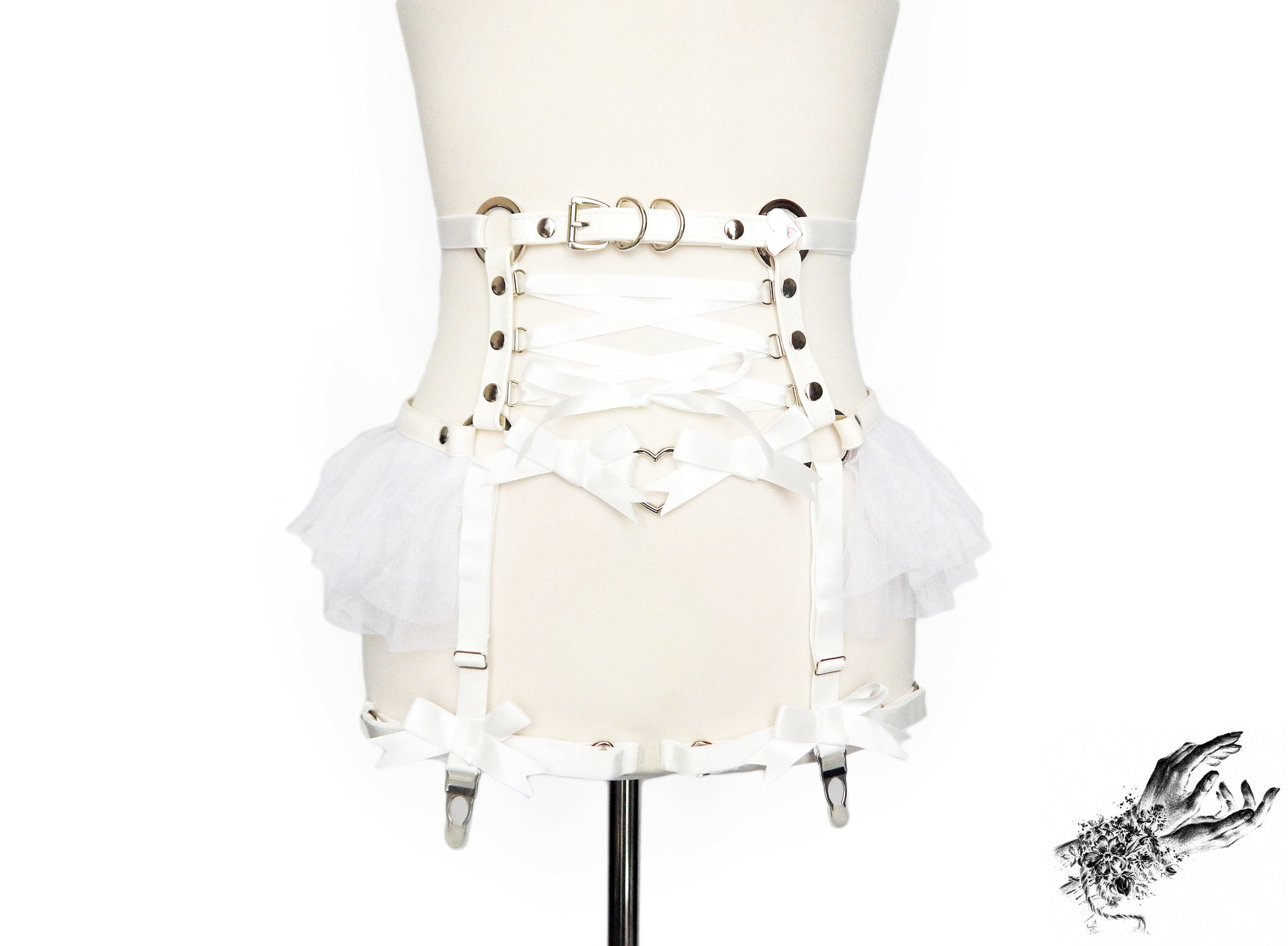 White faux leather garter belt featuring silver heart ring hardware, white ruffled tulle and corset lacing at the waist, displayed on a mannequin against a white background.