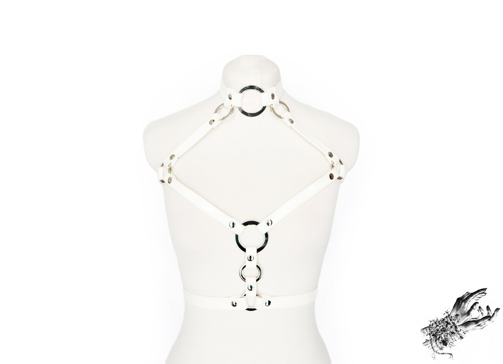 White vegan leather chest harness featuring descending silver O ring hardware and white cross-body straps, displayed on a mannequin against a white background.